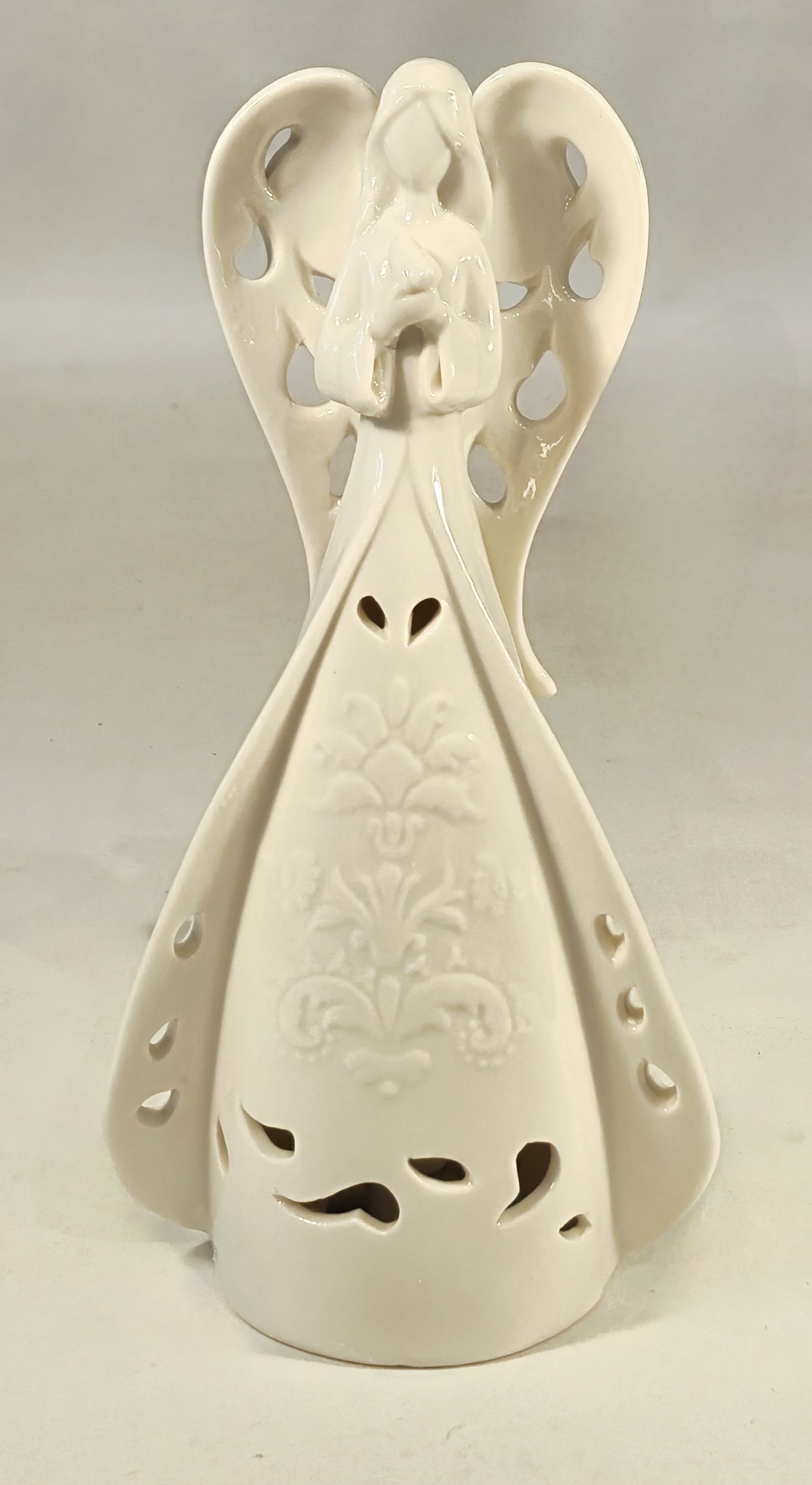 Cream ceramic angel figurine with cutout details and an embossed pattern on the gown.