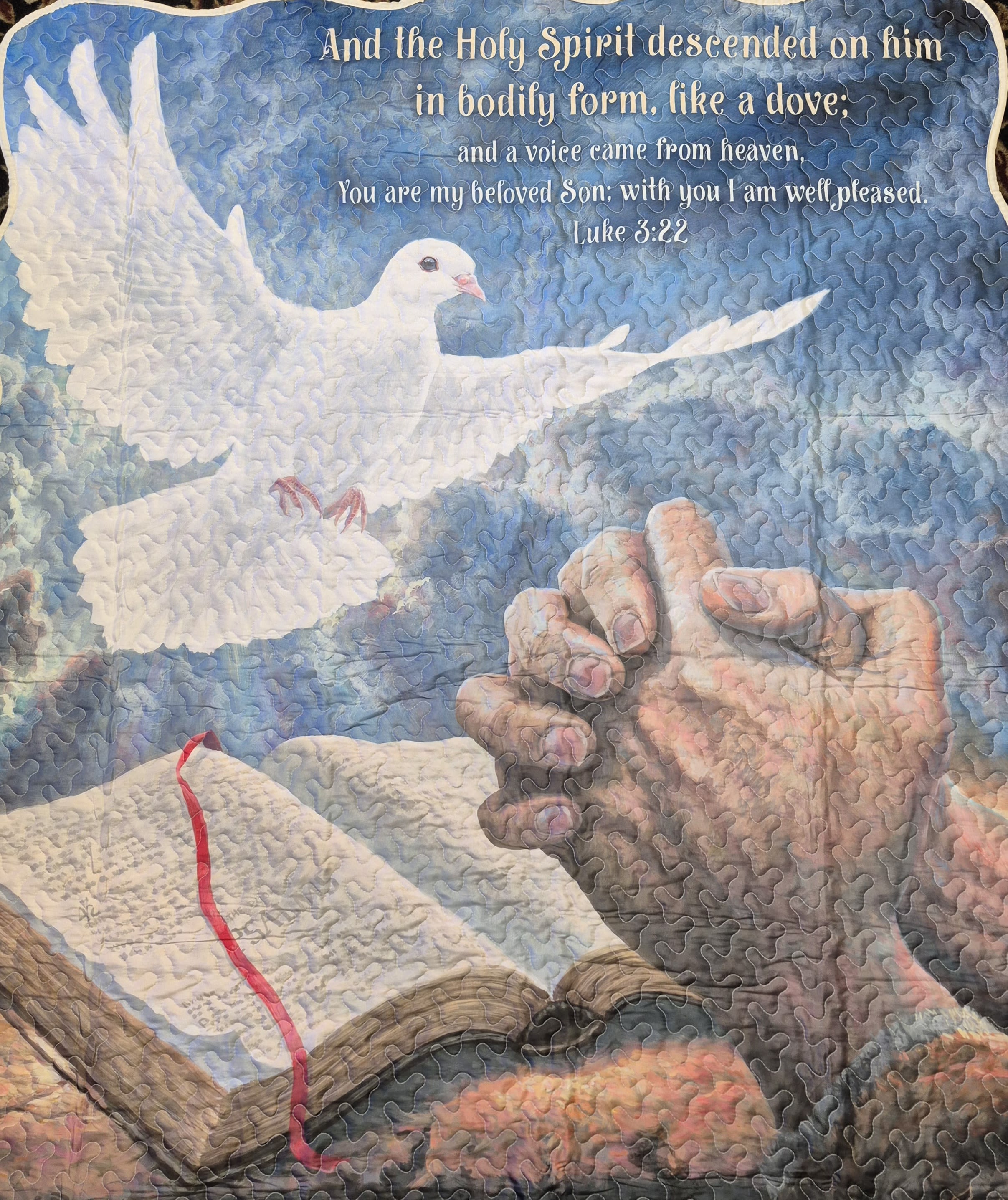 Holy Spirit Luke 3:22 Quilted Throw - A large white dove in flight against a swirling blue sky sets a peaceful, faith-filled tone-this quilted throw is a comforting flower-alternative for sympathy, funeral, or get-well occasions that quietly honors spiritual care. The scripture from Luke 3:22 and the praying hands beside an open Bible communicate solace and presence, making this arrangement-style gift especially fitting for memorial services, a bedside reminder during recovery, or an Easter or Passover remembrance.  The 50" x 60" quilted blanket features a visible stitch pattern that adds handcrafted texture and warmth; colors include calming blues with accents of white, peach, red and mixed tones in the artwork. It arrives with a matching bow for presentation and can be machine washed for easy care-lightweight yet durable for repeated use. For a hands-on display at services or in the home, choose the Deluxe option to add the slender metal easel (available for an additional charge) so the piece can be presented upright as a memorial panel or devotional focal point.