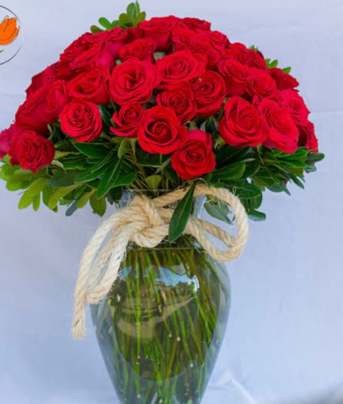 Red roses arranged in a clear glass vase with a rope bow