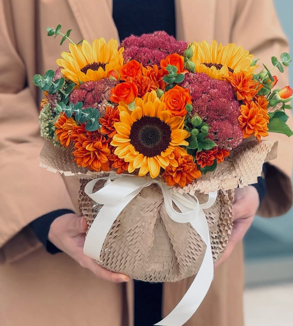 Bouquet of sunflowers, orange roses, and burgundy blooms wrapped in kraft paper