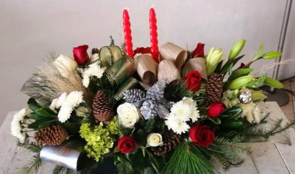 Christmas Glows - A festive holiday centerpiece featuring classic red roses, elegant white lilies, textured winter greens, natural pinecones and sparkling accents finished with bold red taper candles for a warm seasonal glow.