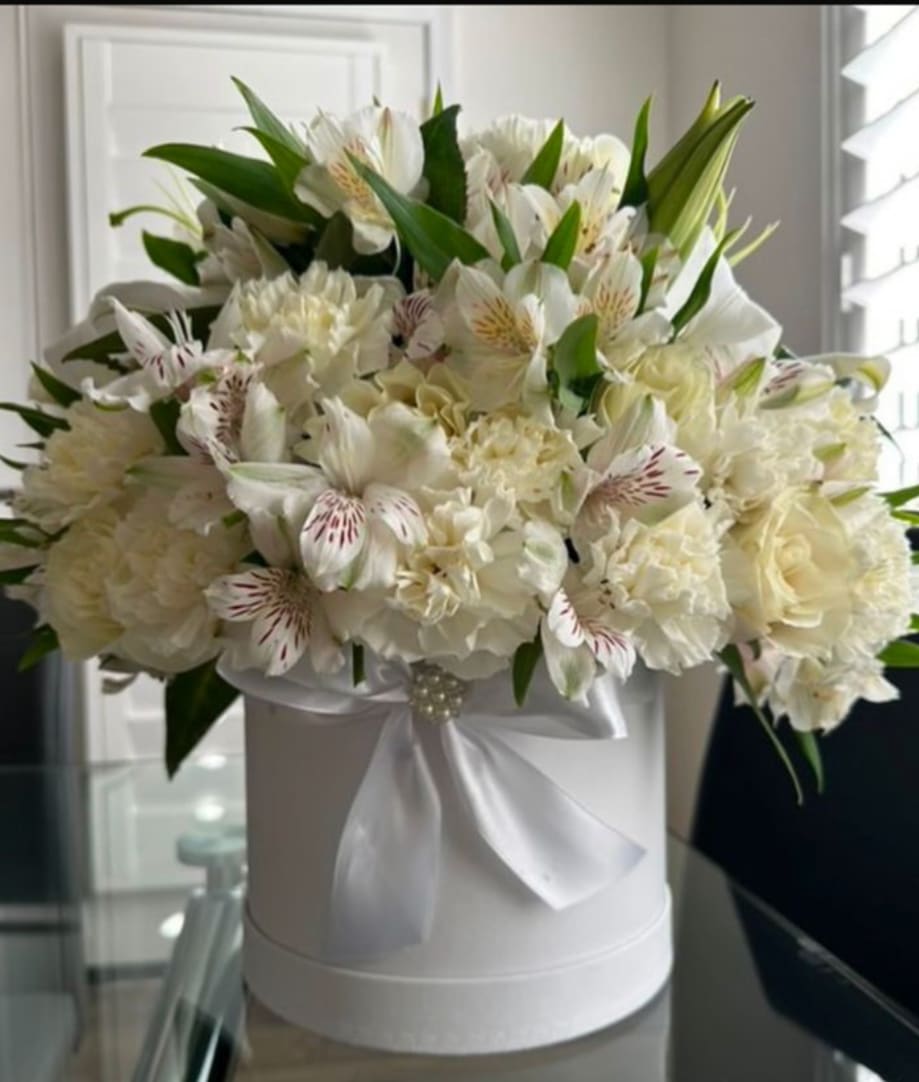 White floral arrangement in a round hat box with a satin ribbon