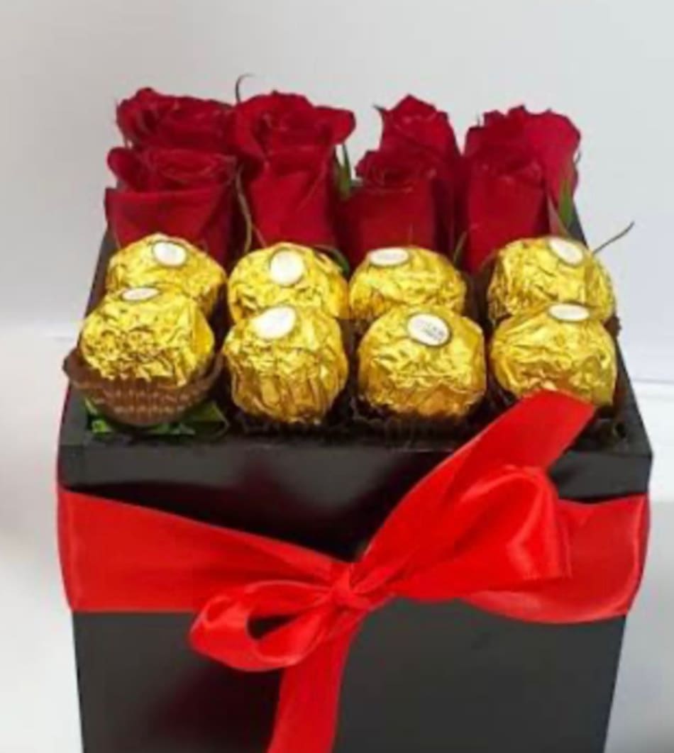 Red roses and gold-wrapped chocolates in a black gift box with a red ribbon