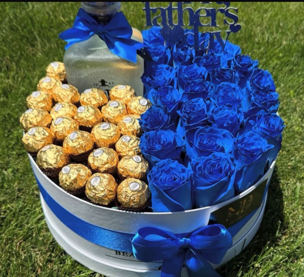 Blue roses and gold-wrapped chocolates arranged in a round gift box with a ribbon.