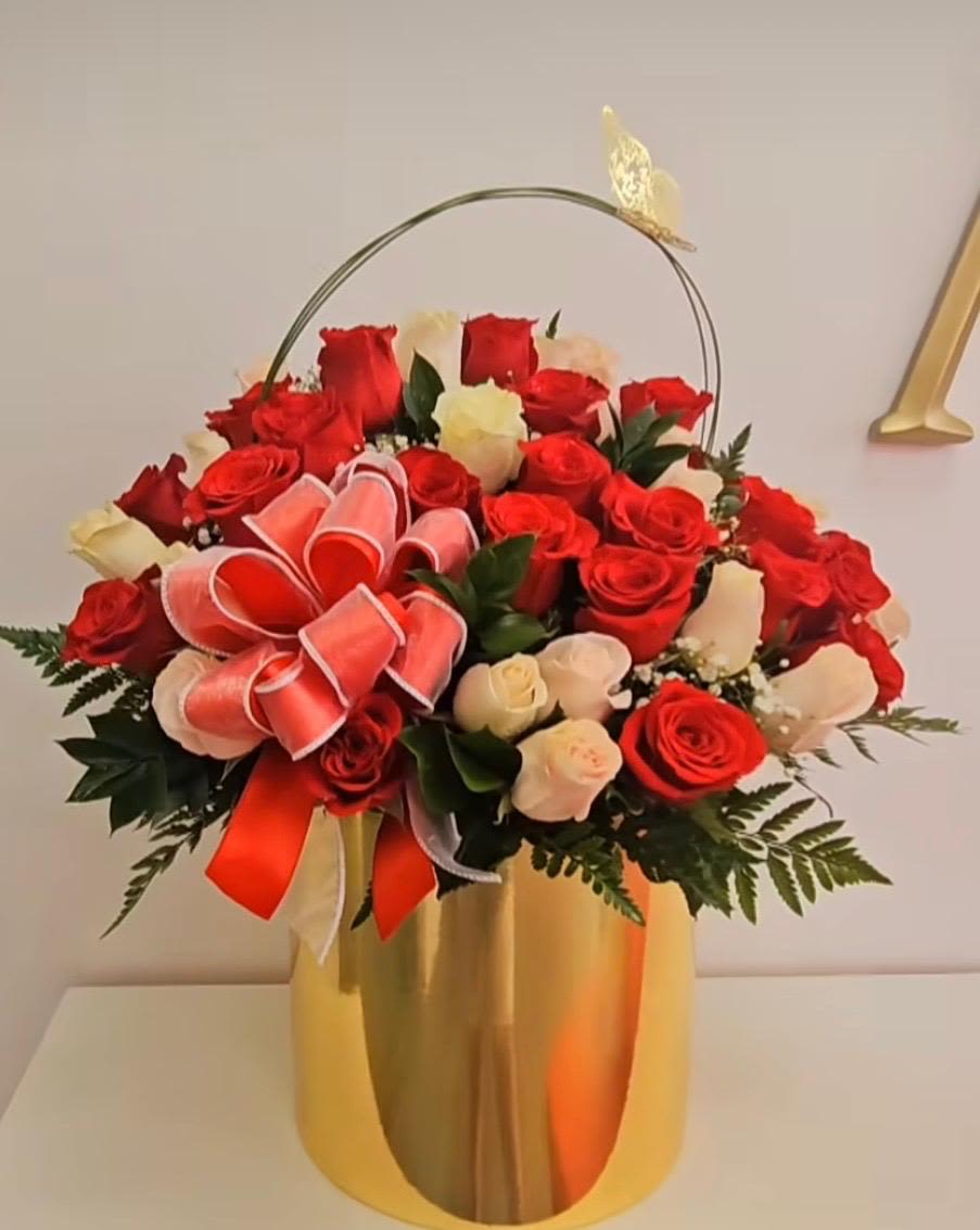Arrangement of red and white roses in a tall gold vase with a ribbon bow and butterfly accent