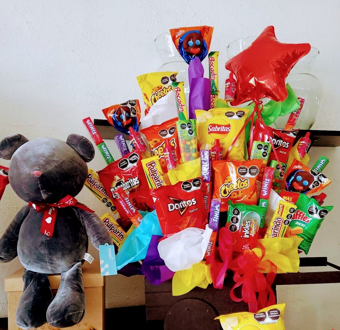Fiesta Snack Celebration Box - Make someone's birthday extra special with our Fiesta Snack Celebration Box, a fun and unique gift basket filled with popular snacks, candies, chips, treats, a plush teddy bear, and festive birthday balloon. Handcrafted by Snyder Flowers in San Antonio, Texas, this creative gift is perfect for birthdays, celebrations, congratulations, get well wishes, graduations, employee appreciation, kids' gifts, teen birthdays, surprise deliveries, and special occasions. We proudly offer same-day gift basket delivery throughout Stone Oak, Alamo Heights, The Dominion, Shavano Park, Helotes, Medical Center, Schertz, Cibolo, Boerne, Leon Valley, and surrounding San Antonio areas. If you're searching for birthday gifts near me, snack baskets, candy bouquets, gift delivery, or unique celebration gifts, this colorful arrangement is designed to bring smiles and unforgettable moments.