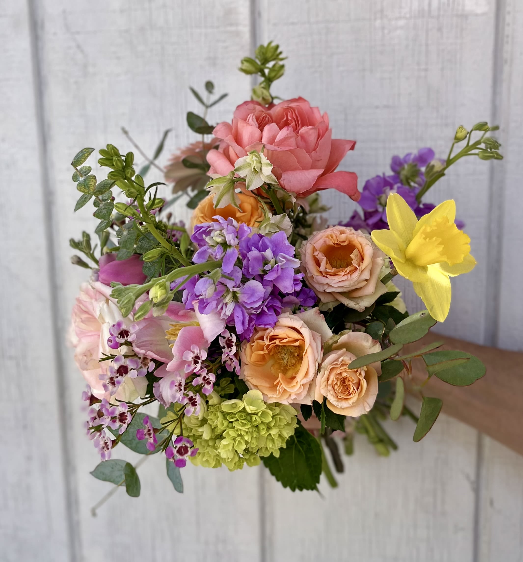 Handheld bouquet of pink, peach, purple, and yellow flowers