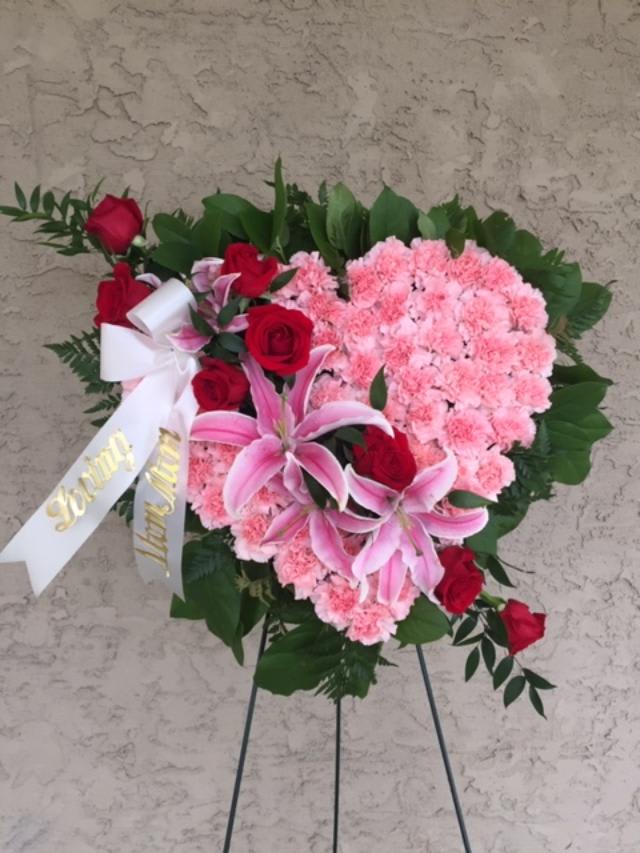 Heart-shaped floral spray with pink carnations, red roses, and lilies on an easel