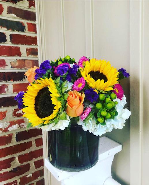 Bright mixed bouquet with sunflowers, roses, and daisies in a dark vase