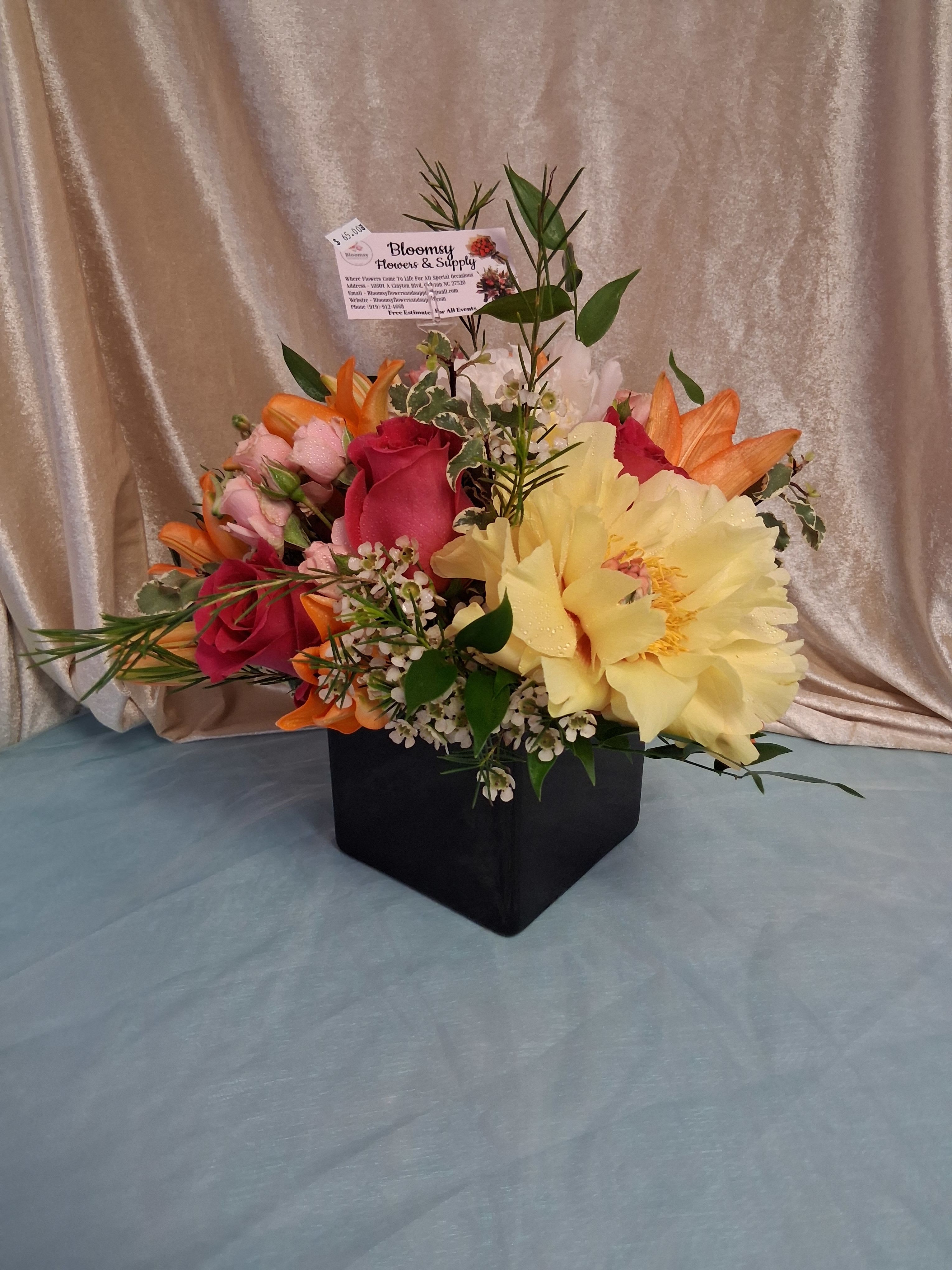 Elegant Peony Arrangement  - A lush cluster of pink roses and vibrant orange lilies makes this flower arrangement feel joyful and intimate-the perfect birthday bouquet or thank-you gift that reads both celebratory and romantic. The compact black square vase and included floral pick card give it a polished, gift-ready presentation that will make the person you're thinking of feel truly celebrated.  This arrangement combines pale yellow blooms, small white filler flowers, and variegated foliage around the larger roses and lilies for a textured, textural contrast that catches the eye from every angle. The low, dense design sits in a modern black square vase that keeps stems neatly concealed while letting the colors pop-pink, yellow, orange, and white play together for a fresh, sunny palette.  Send this to mark birthdays, send thanks, or brighten someone's day with a bouquet that reads thoughtful and refined. Vase is included and arrives ready to display; the floral pick card is added for your personal message.