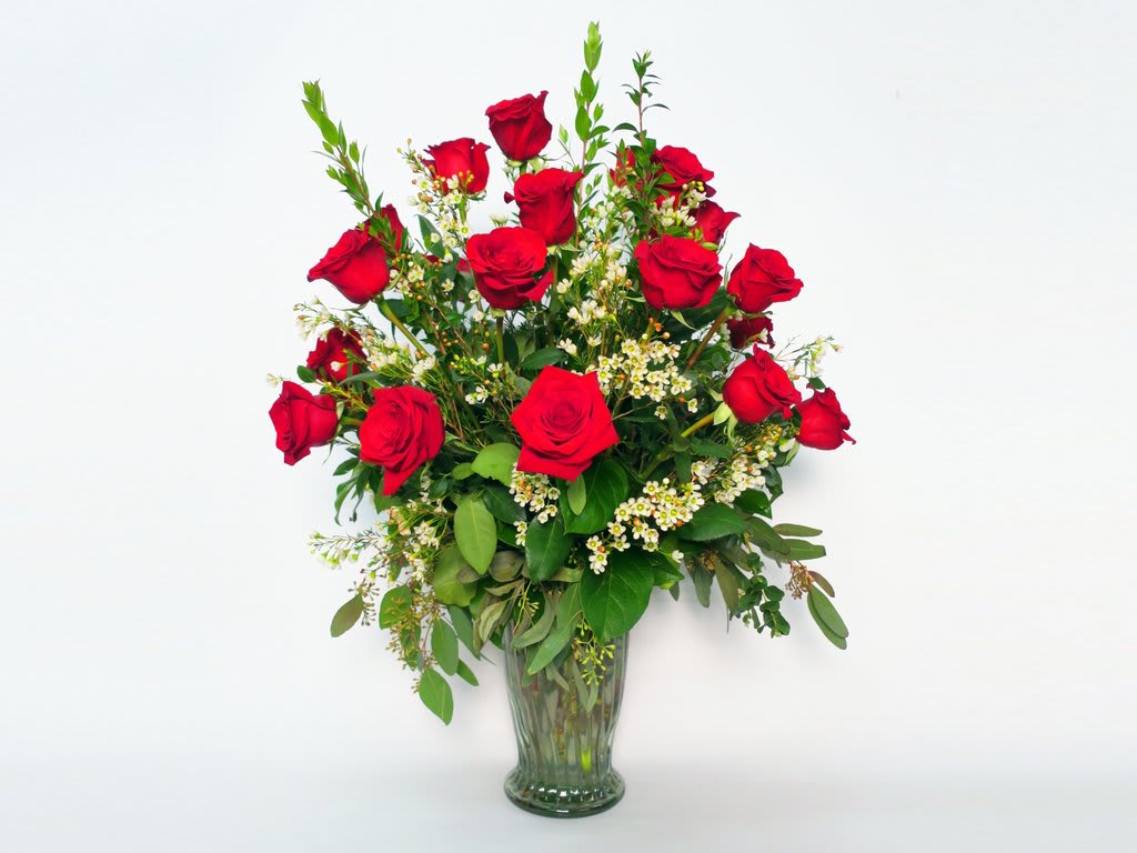 Red roses arranged in a clear glass vase with small white filler flowers