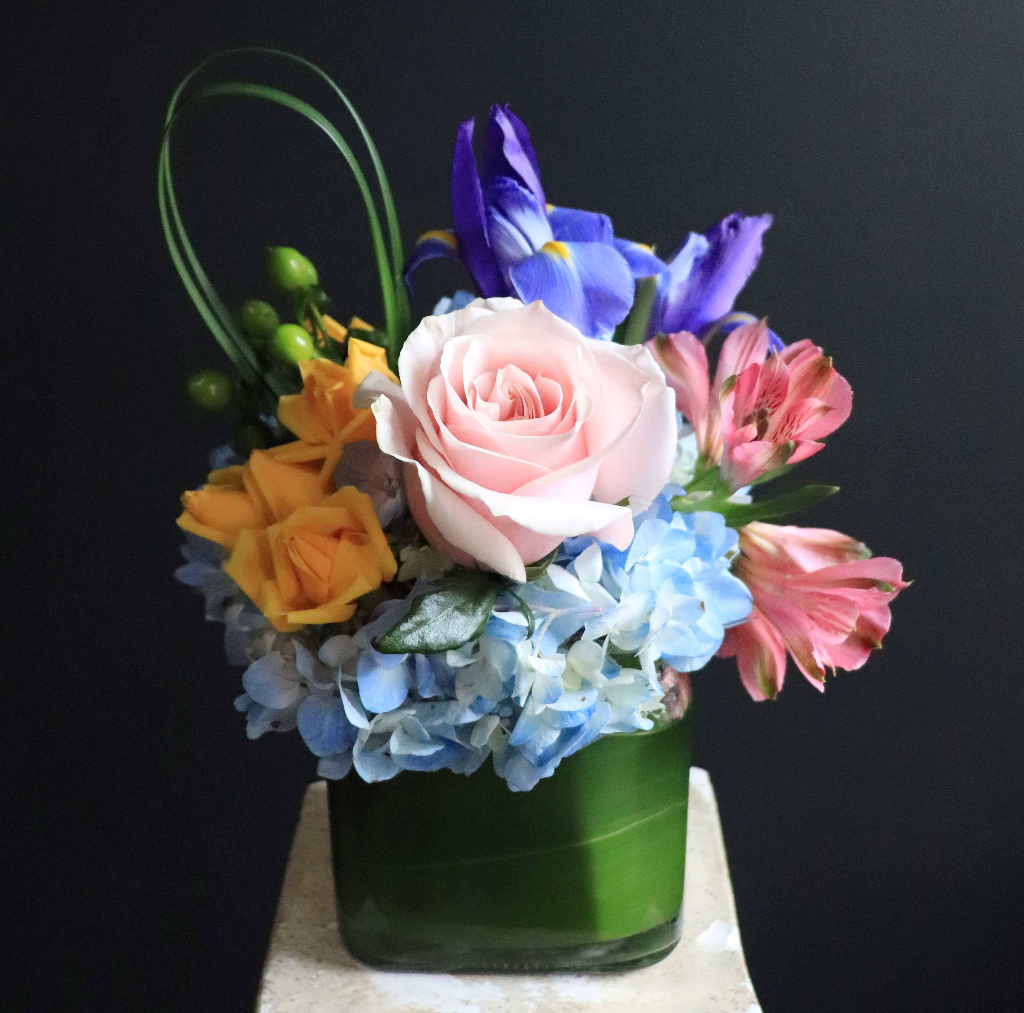 Celebrating You - Quite the joyful arrangement to celebrate someone you care about! Full of soft colors and life in a glass cubed vase lined with an aspidistra leaf, this small arrangement is bursting with fun and style!