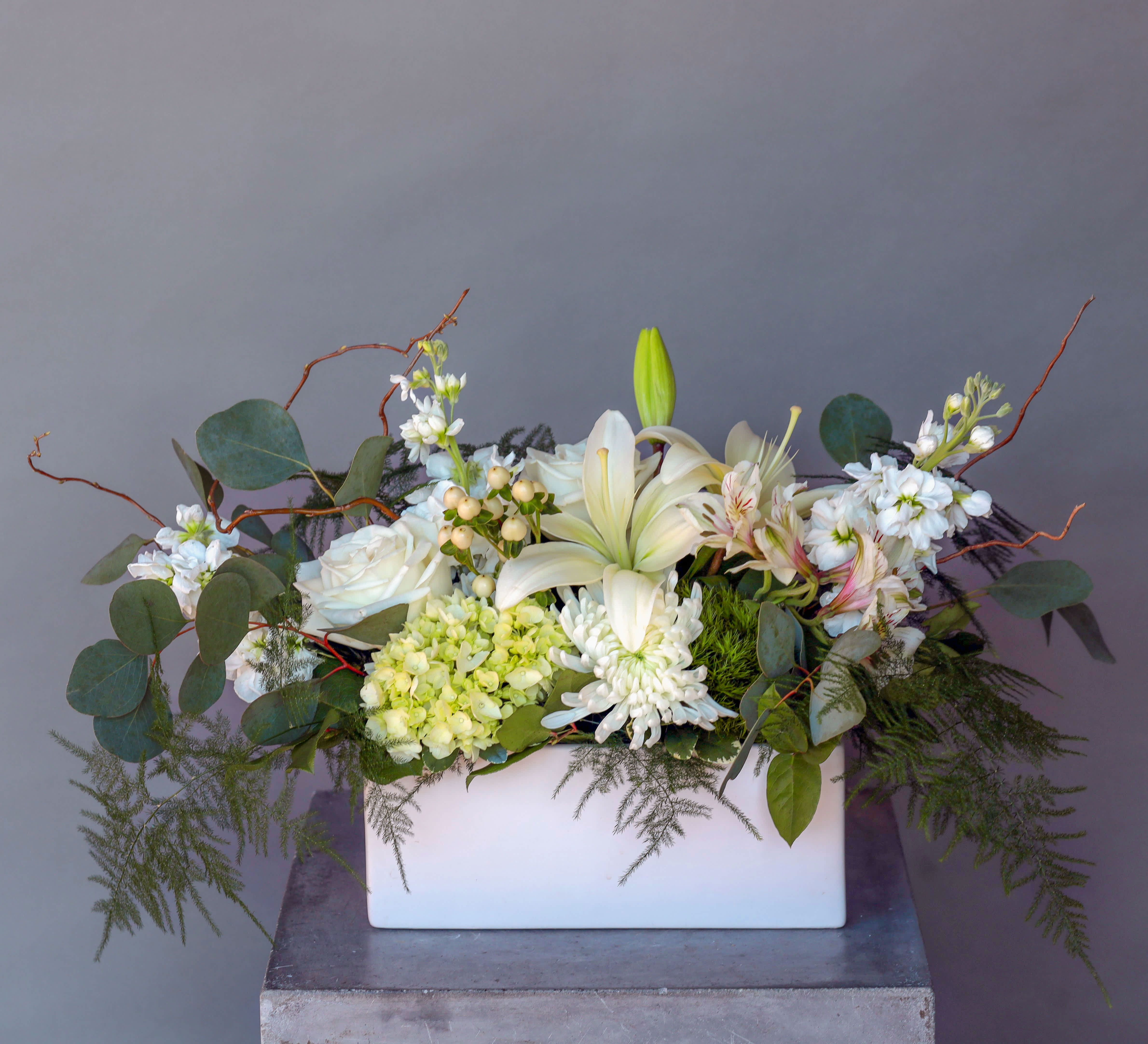 Comforting Wishes - Express your deepest condolences with the serene beauty of the "Comforting Wishes" arrangement. This elegant display features an abundance of pristine white flowers, symbolizing purity, peace, and enduring love. Lush greenery adds a touch of tranquility, creating a thoughtful tribute that offers solace to grieving hearts.