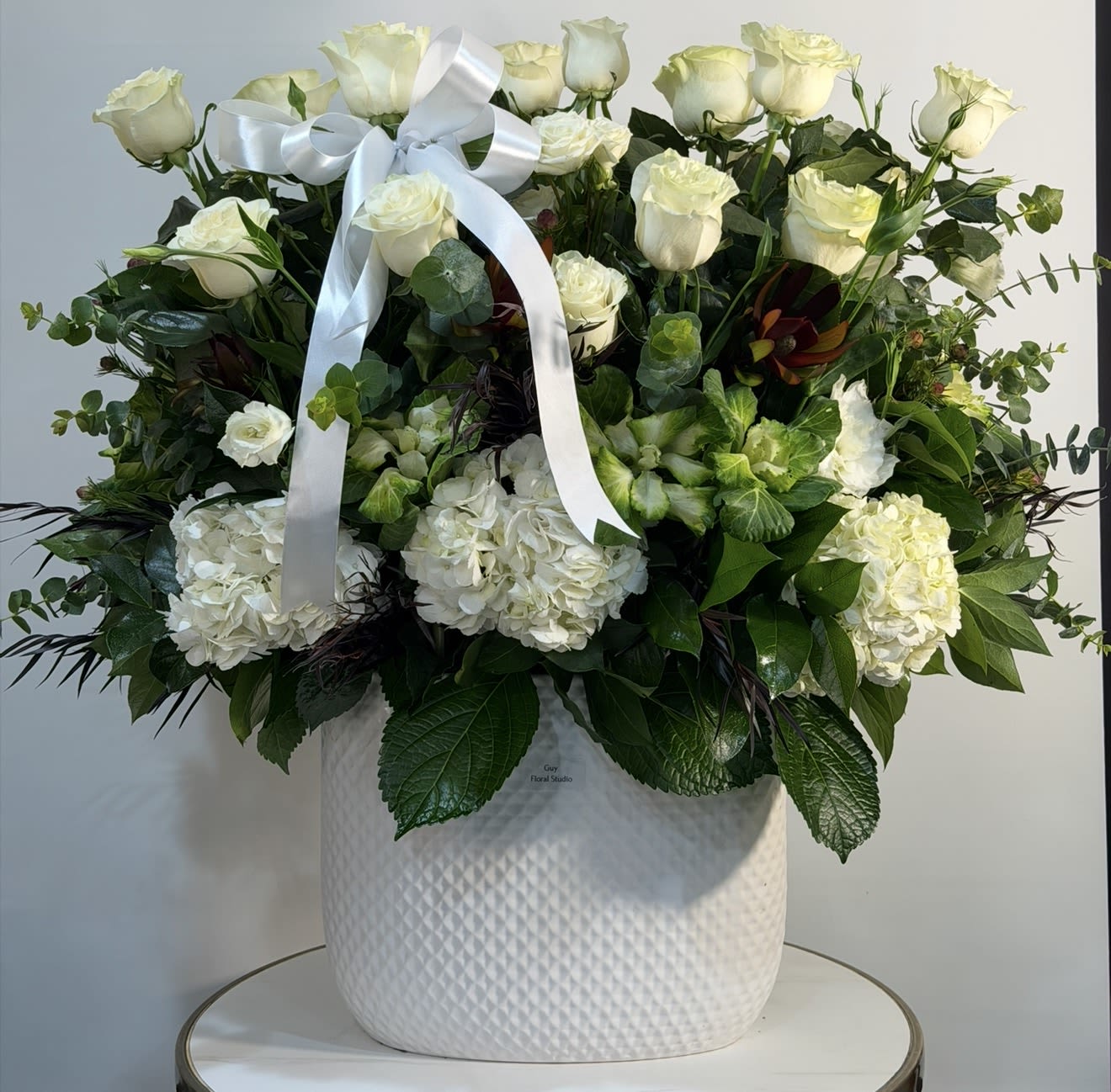 Grand Ivory Elegance - A large and luxurious white floral arrangement designed to impress. “Grand Ivory Elegance” features premium white roses, lush hydrangeas, and fresh seasonal greenery, beautifully arranged in a modern ceramic vase for a clean and sophisticated look. This stunning design is perfect for sympathy, condolences, upscale events, or anyone who appreciates timeless beauty and elegance. The full, rich composition creates a grand presence, making it an ideal centerpiece or meaningful gift. Handcrafted with care at Guy Floral Studio, each arrangement is made using the freshest flowers to ensure quality and longevity. We offer reliable same day flower delivery in West Hollywood, Beverly Hills, Hollywood, Beverly Grove, Santa Monica, and surrounding Los Angeles areas. Order today for fast and elegant flower delivery.