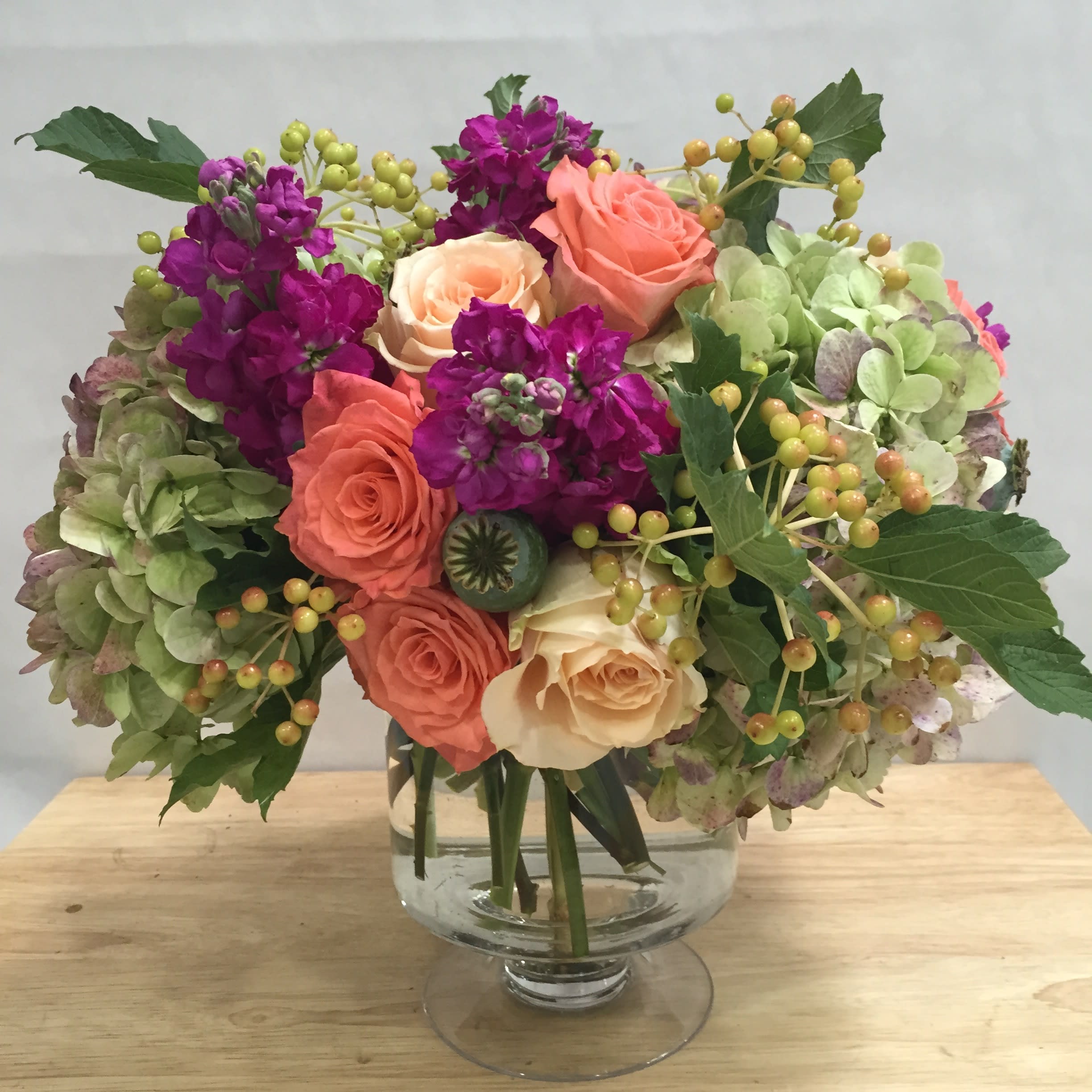 Bouquet of coral and cream roses with purple blooms in a glass vase