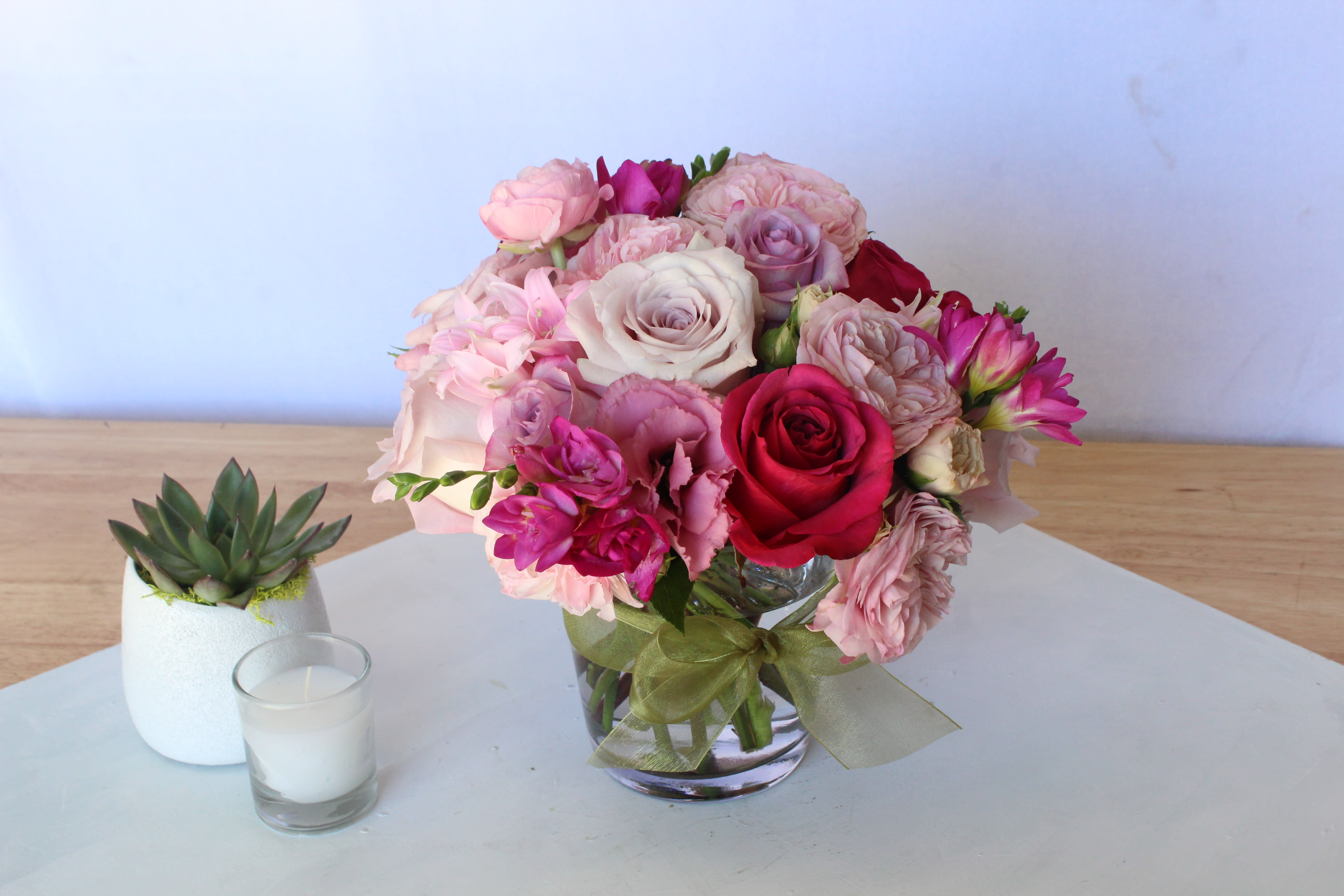 Pink and red rose bouquet in a glass vase beside a small succulent and candle