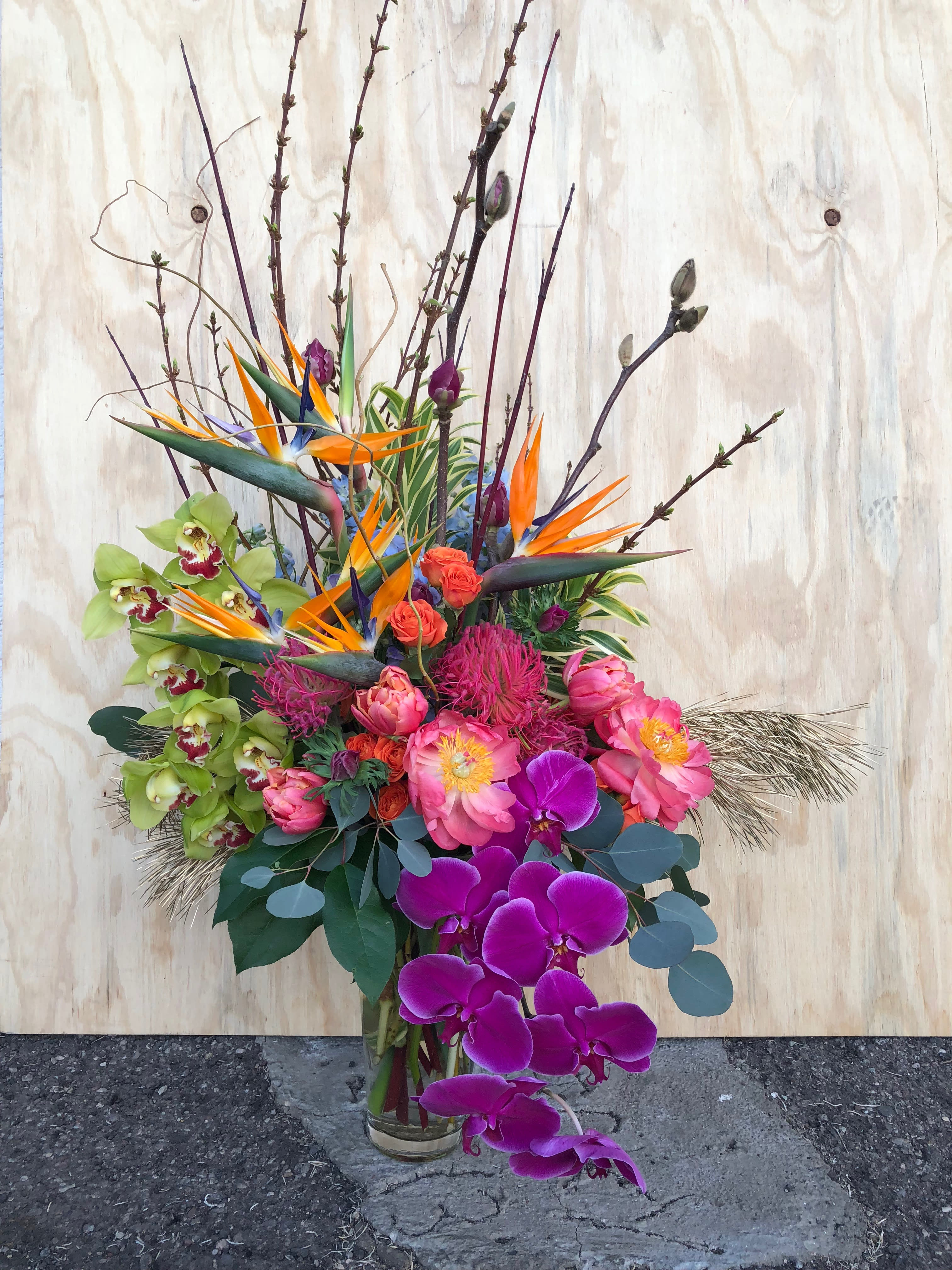 Tall tropical bouquet with orchids, bird of paradise, and pink blooms in a glass vase