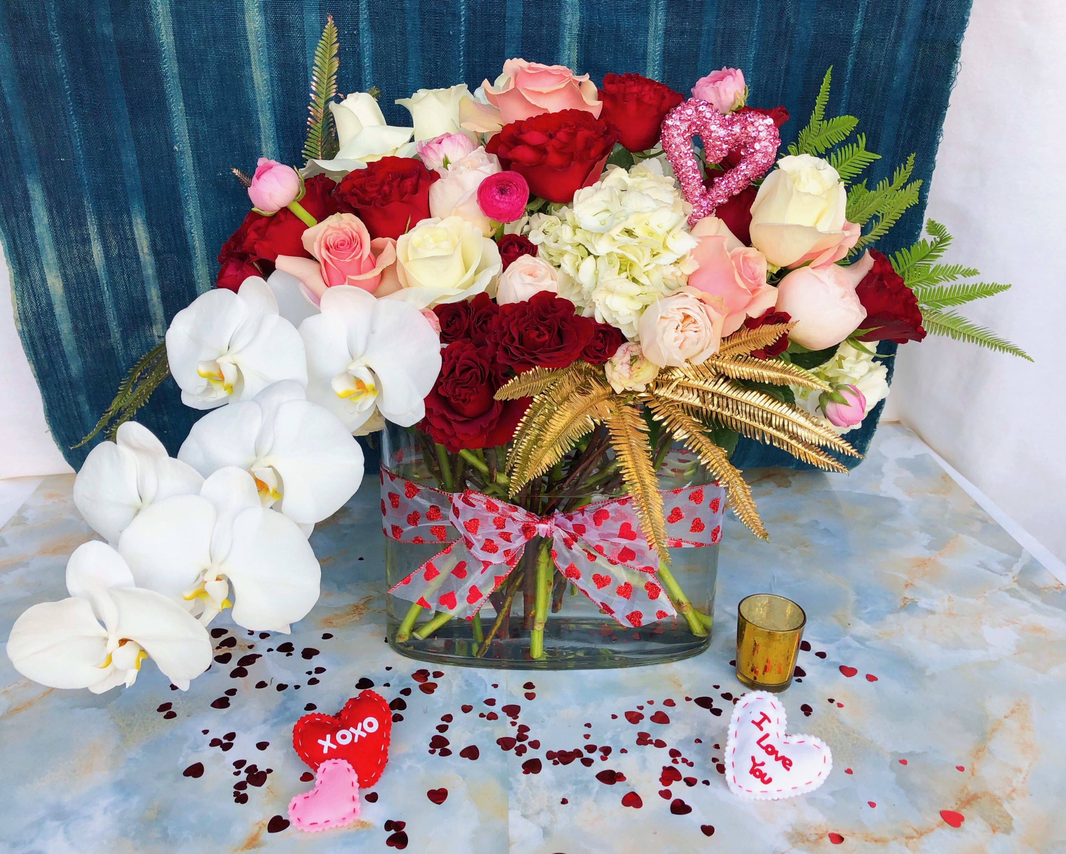 Mixed roses and orchids in a glass vase with heart decorations