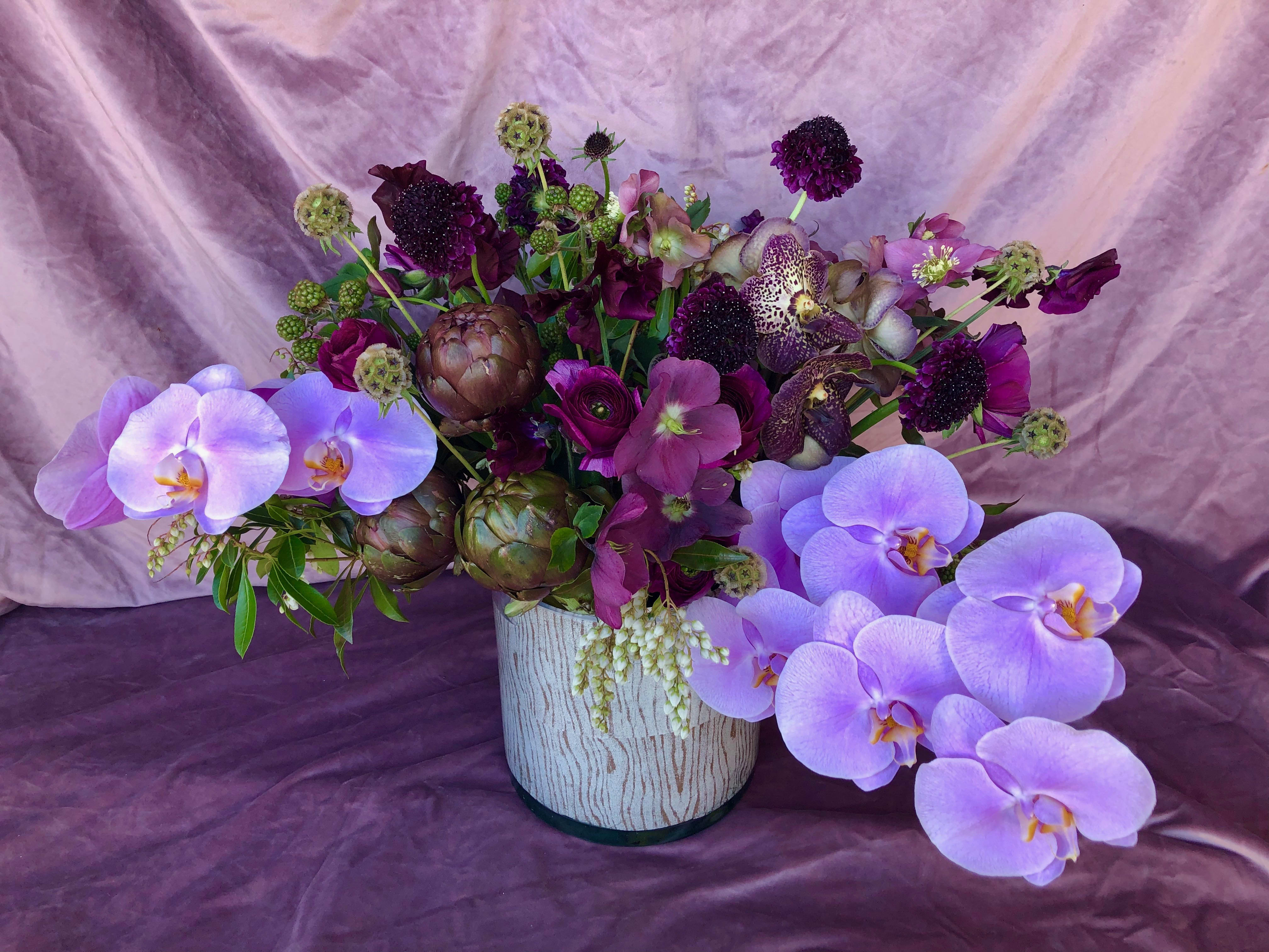Purple floral arrangement with orchids in a white vase