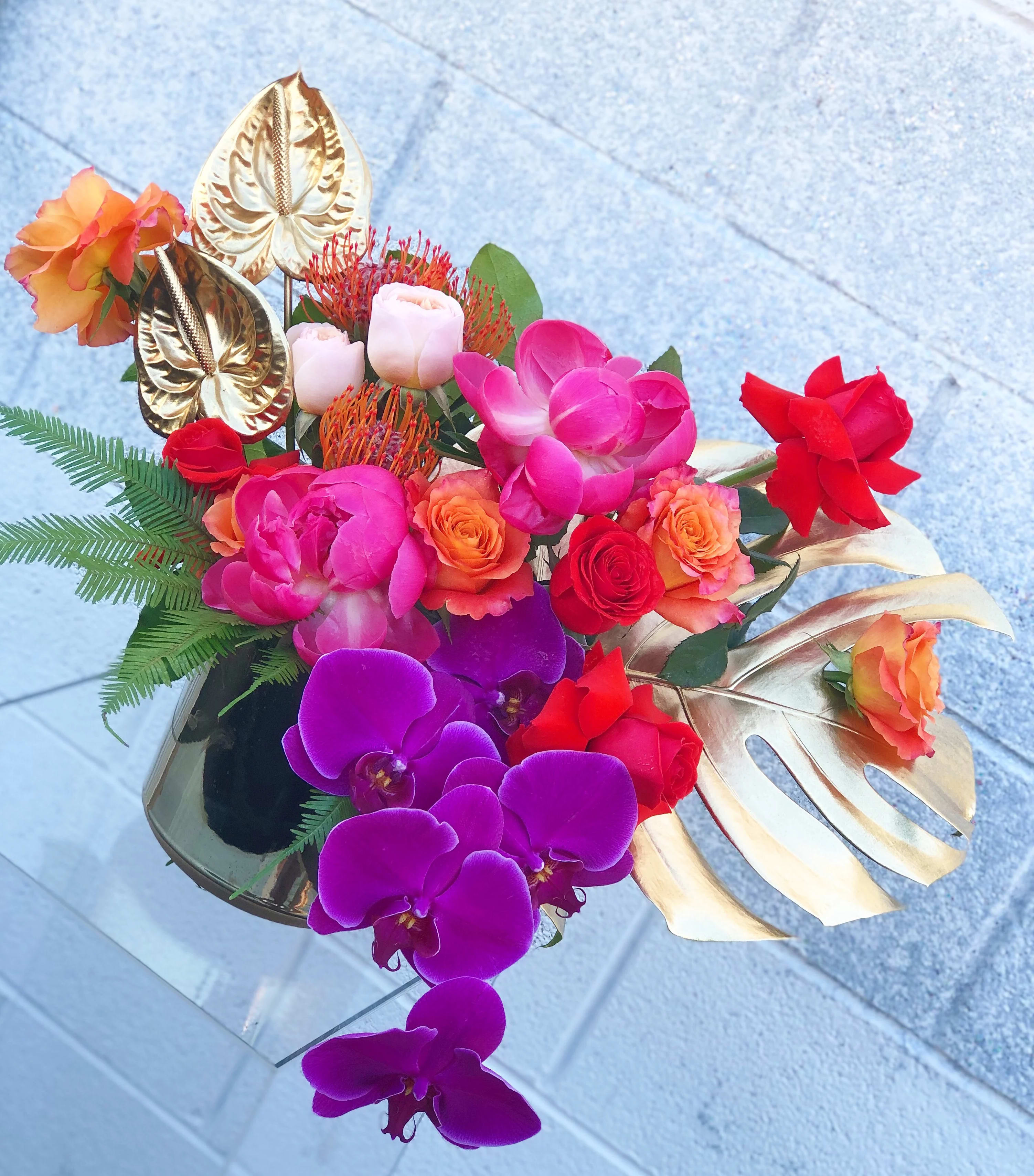 Tropical bouquet with orchids, roses, and gold leaves in a vase