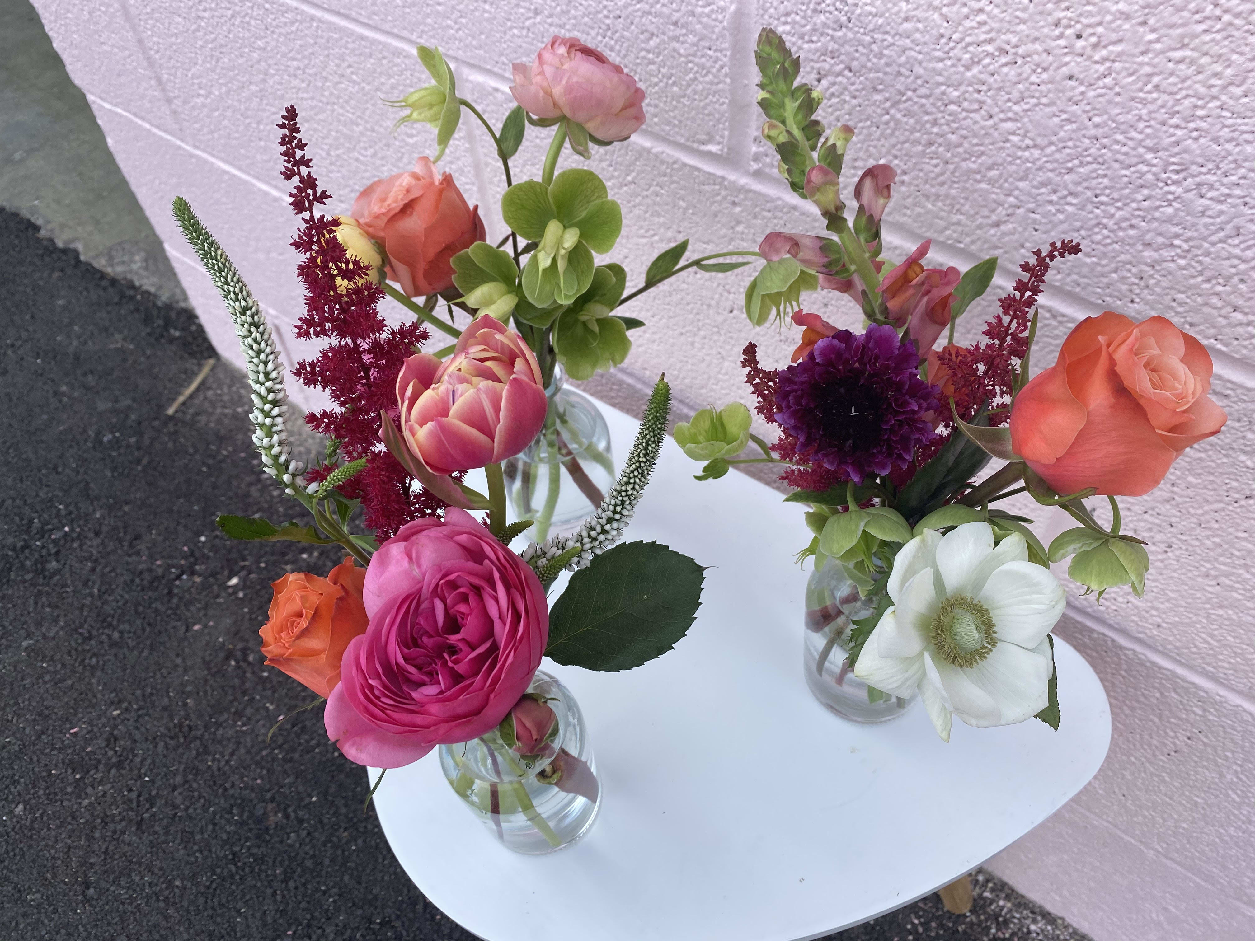 Three small mixed flower arrangements in clear glass vases on a white table.