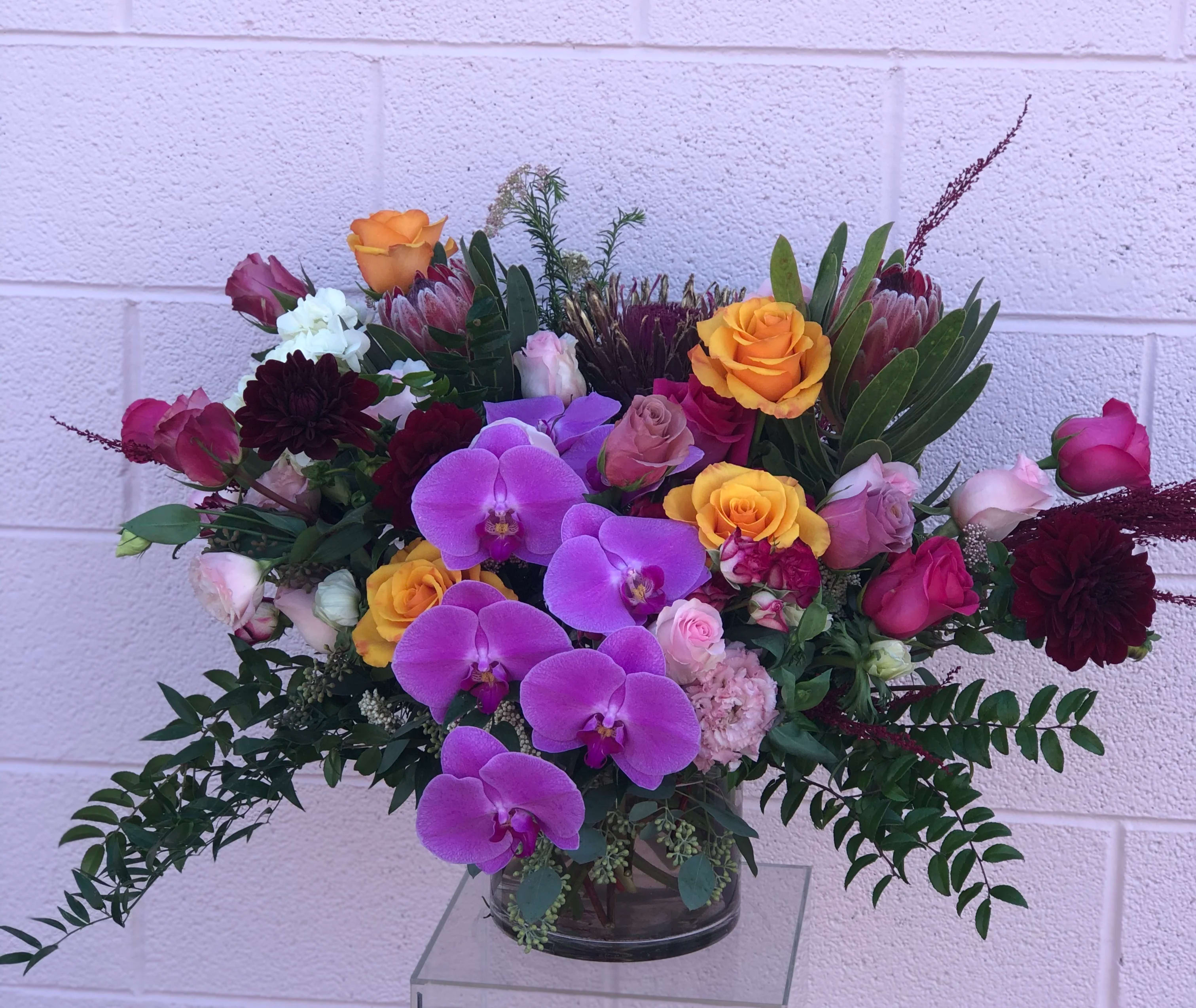 Mixed bouquet with purple orchids, yellow roses, and burgundy blooms in a glass vase