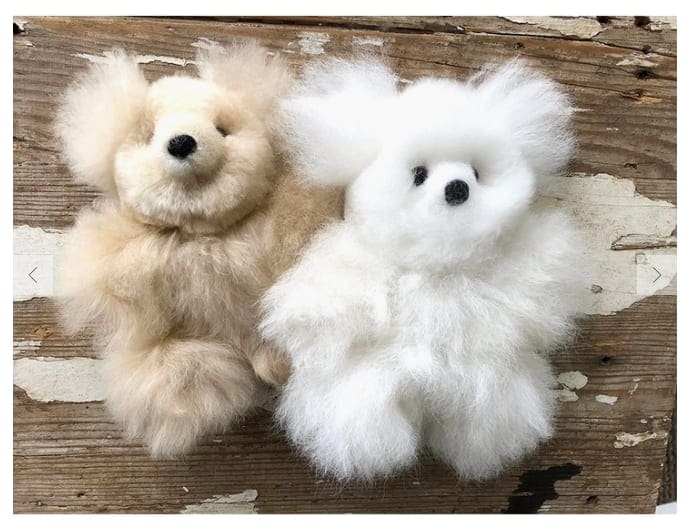 Two fluffy teddy bears, one beige and one white, on a wooden surface.