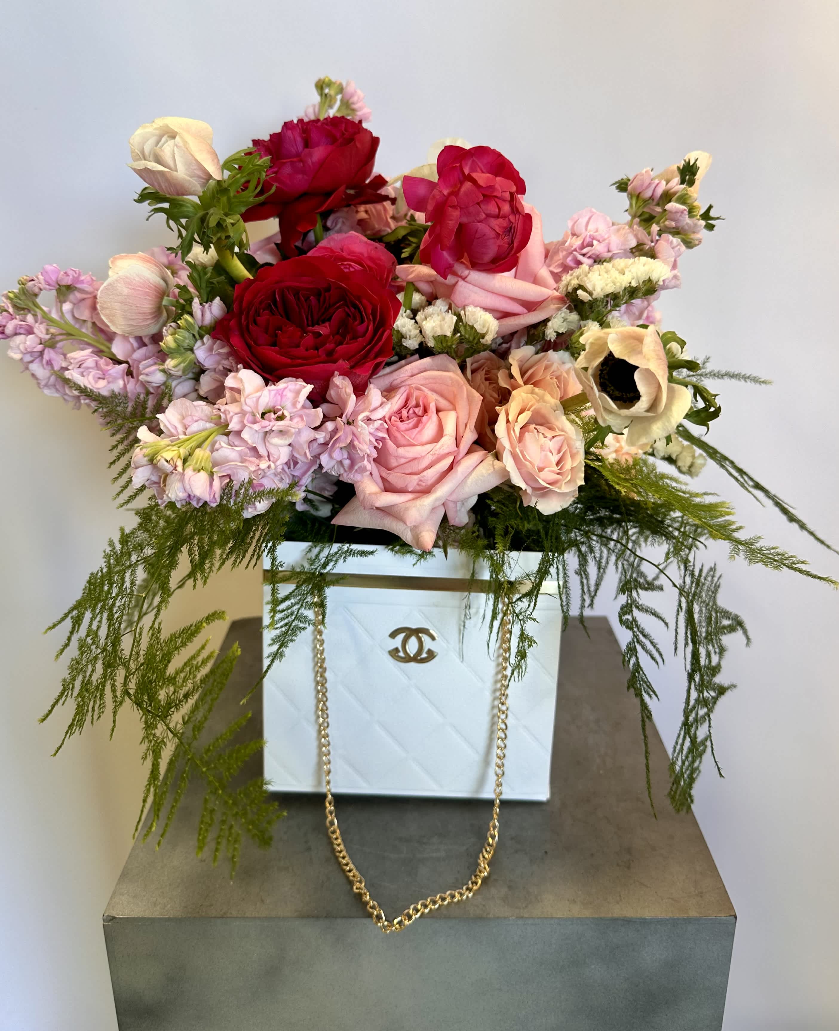 Mixed pink and red roses arranged in a white box with trailing greenery