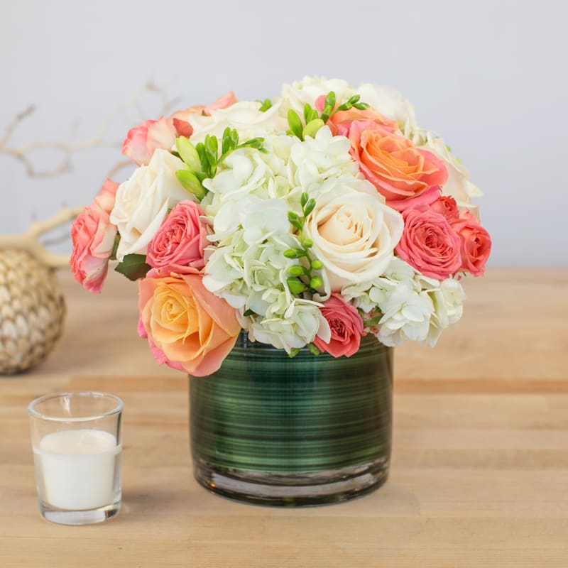 Bouquet of pink, peach, and white roses in a green glass vase