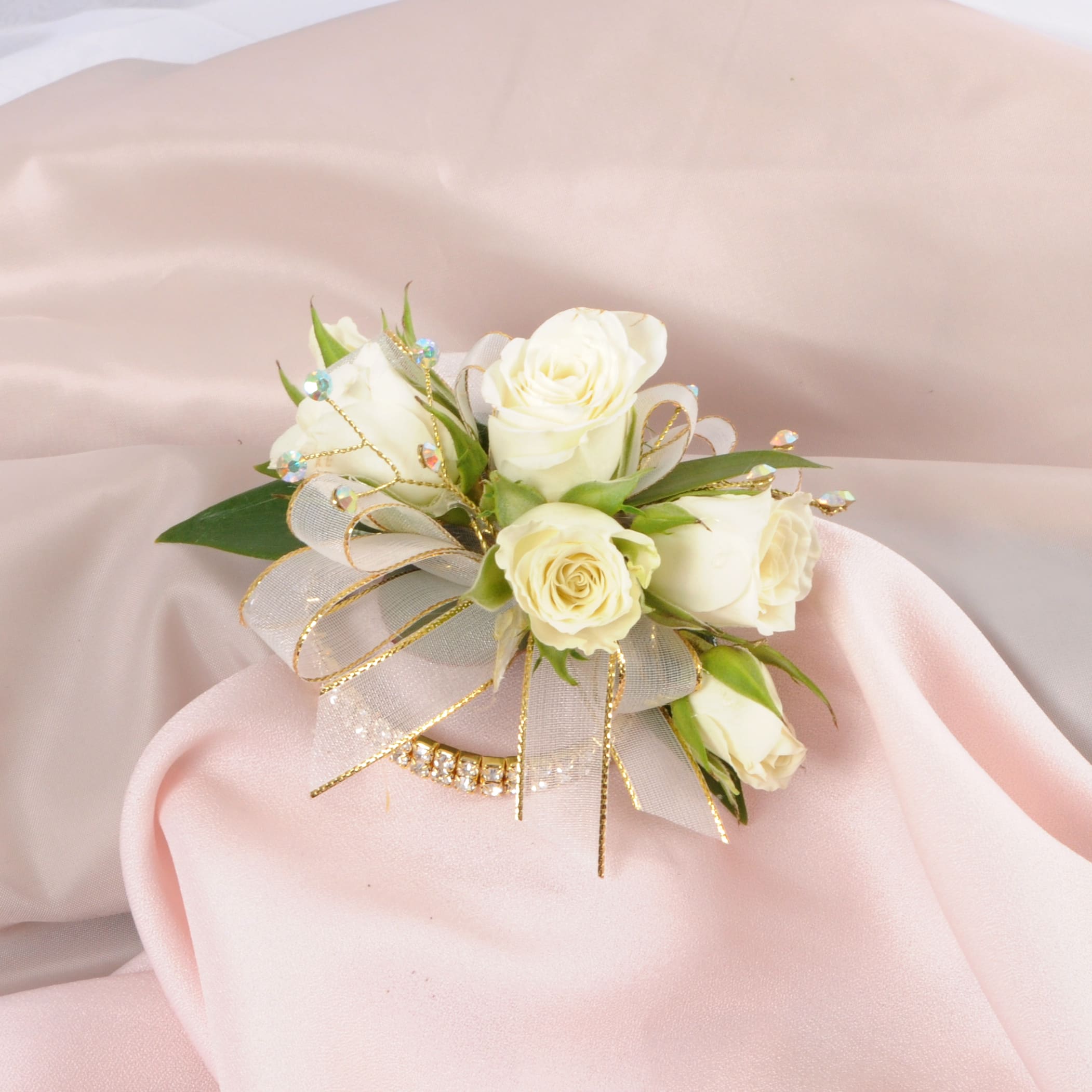 White rose wrist corsage with gold ribbon on soft pink fabric.