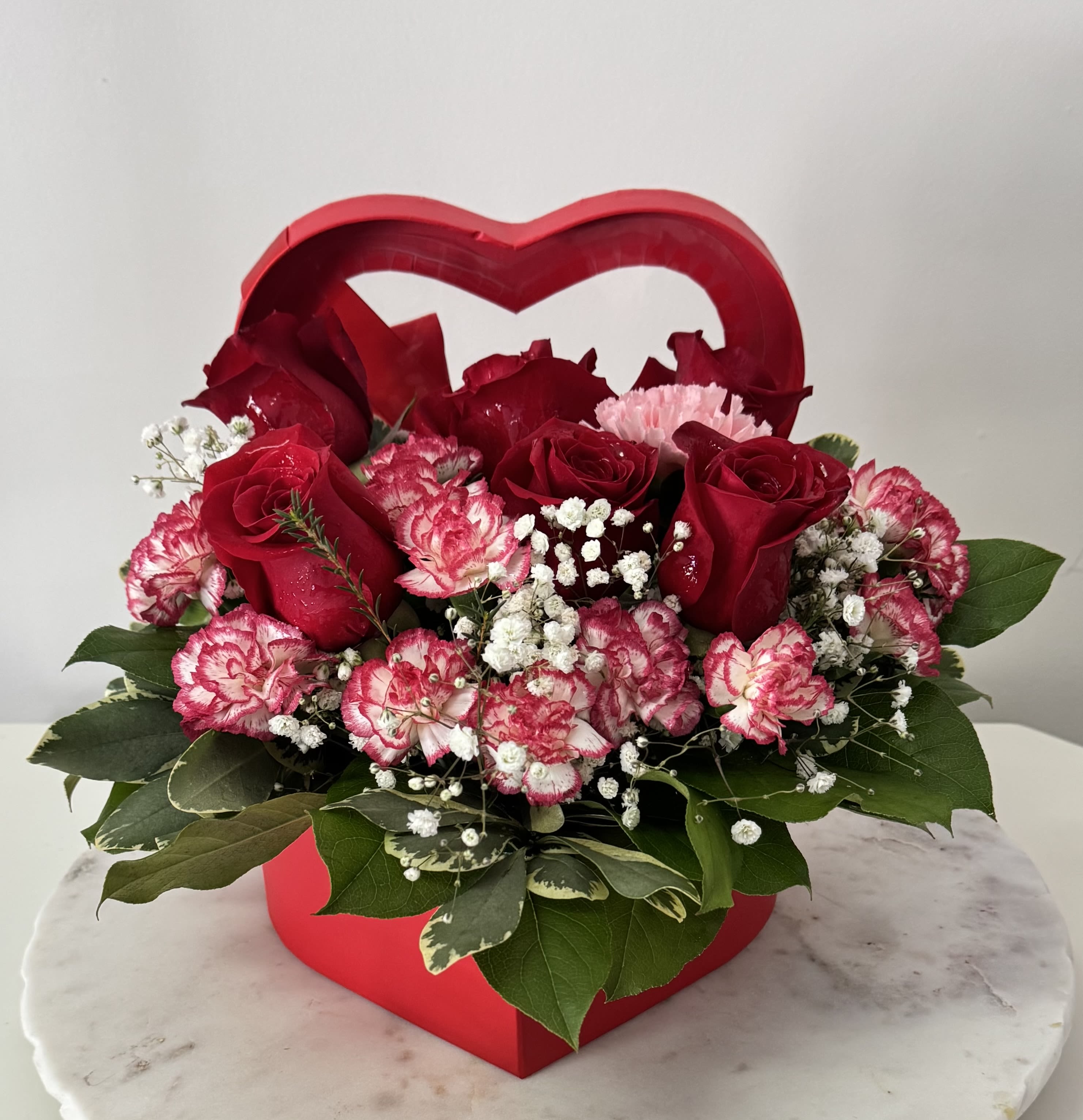 Heart-shaped red box filled with red roses and pink carnations