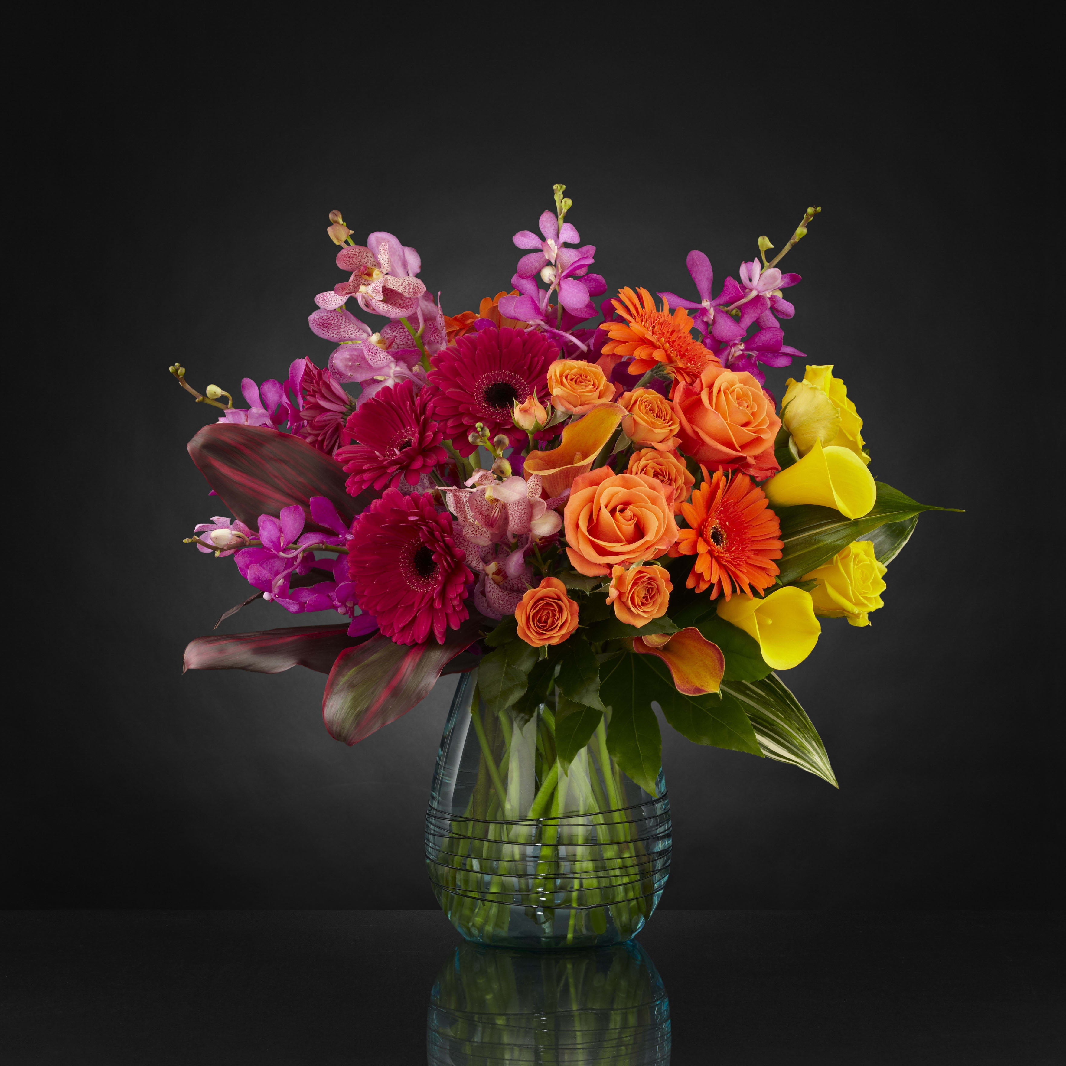Colorful bouquet of roses, gerbera daisies, orchids, and calla lilies in a glass vase