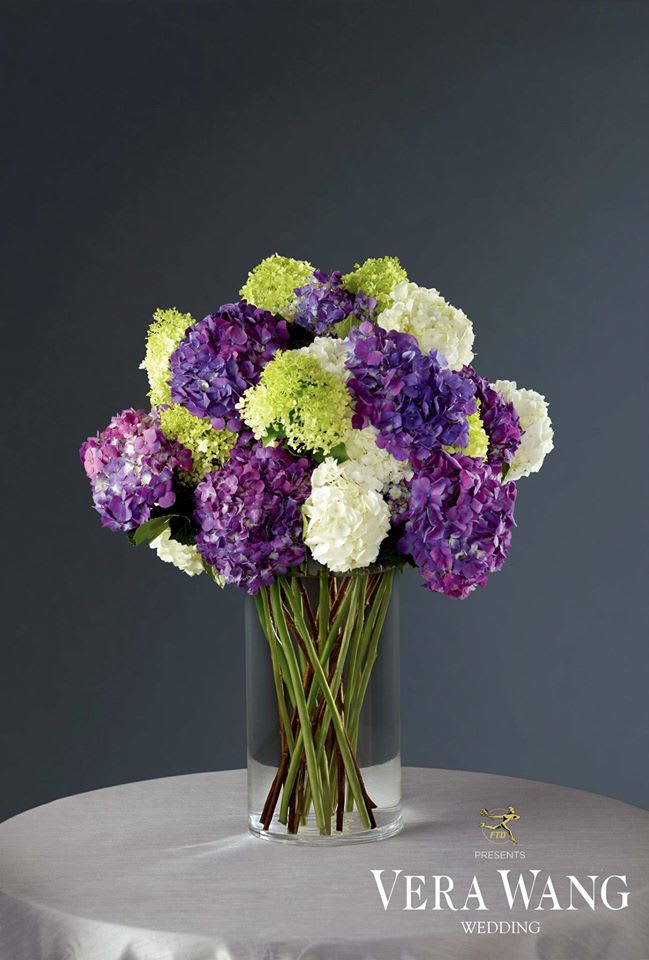 Purple, white, and green hydrangeas in a clear glass vase