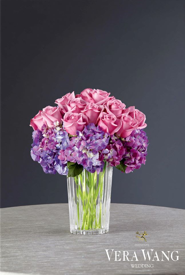 Pink roses and purple hydrangeas arranged in a clear glass vase.