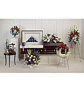 Patriotic funeral floral tributes around a casket with red, white, and blue flowers