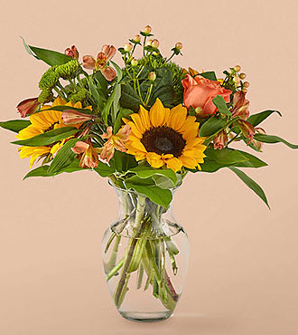 Sunflowers and peach roses arranged in a clear glass vase