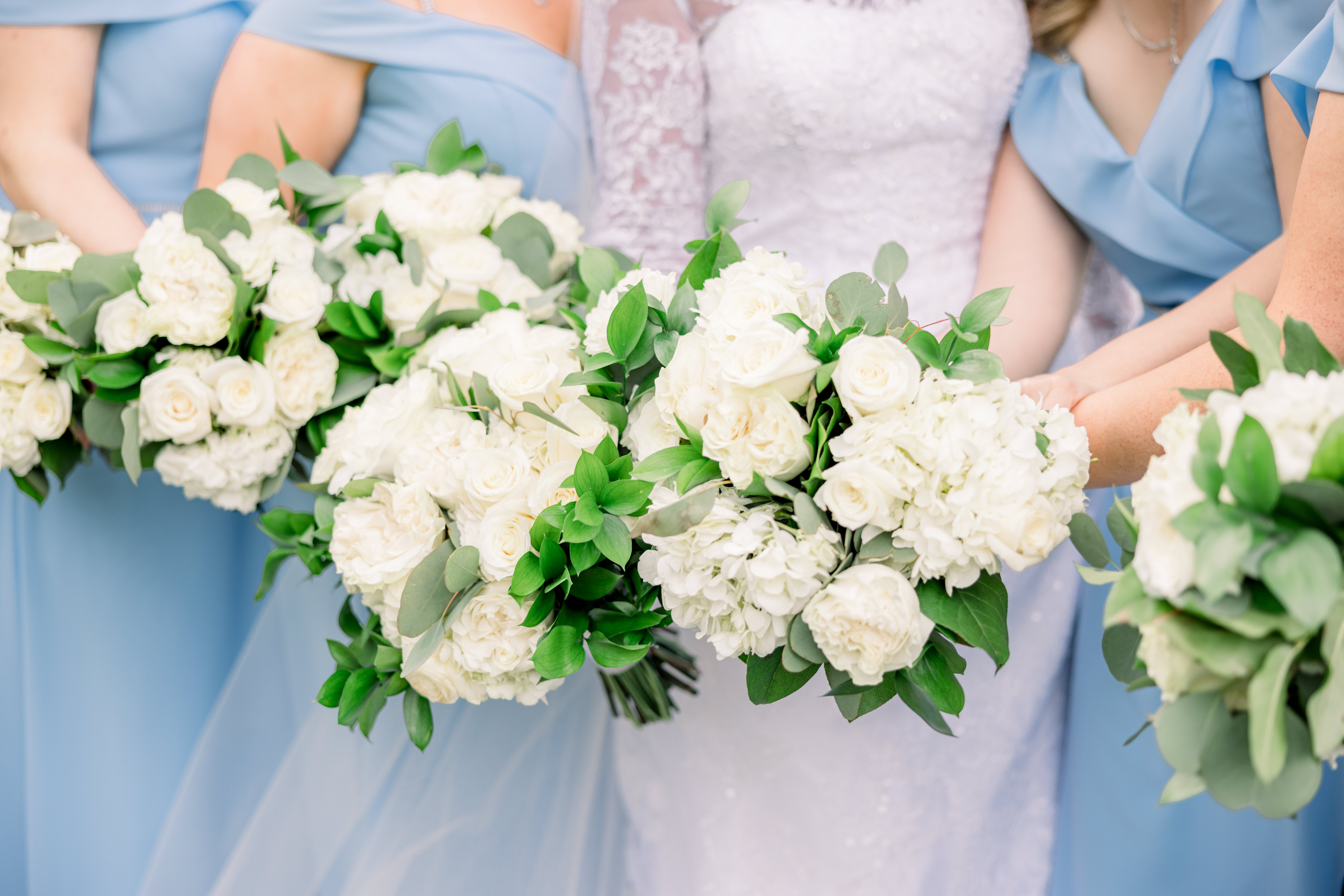Bridesmaids holding white rose bouquets with greenery