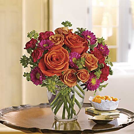 Orange roses and magenta daisies in a clear glass vase