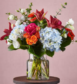 Mixed bouquet of roses, hydrangeas, and lilies in a clear glass vase