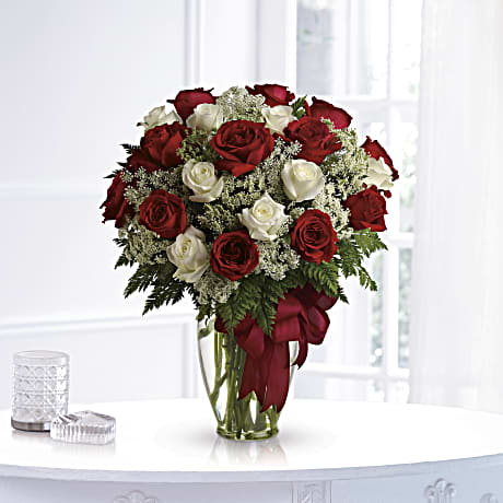 Red and white roses arranged in a clear glass vase with a red ribbon
