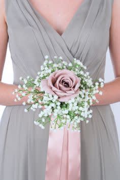 Bridesmaid holding a pink rose wrist corsage with baby's breath and ribbon