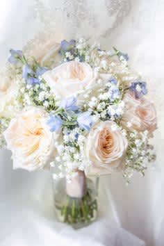 Blush and white rose bouquet in a glass vase with small blue flowers
