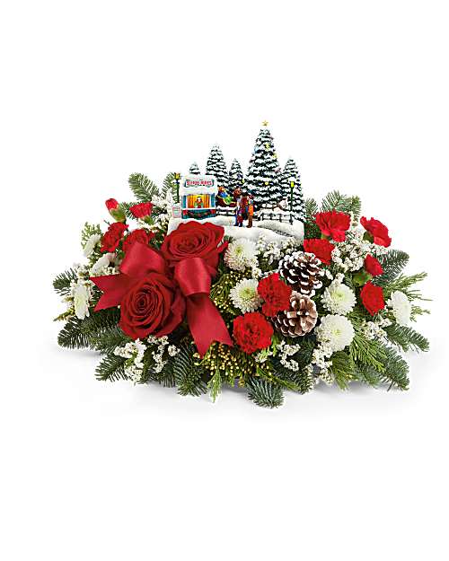 Christmas floral arrangement with red roses, pinecones, and a small winter village scene