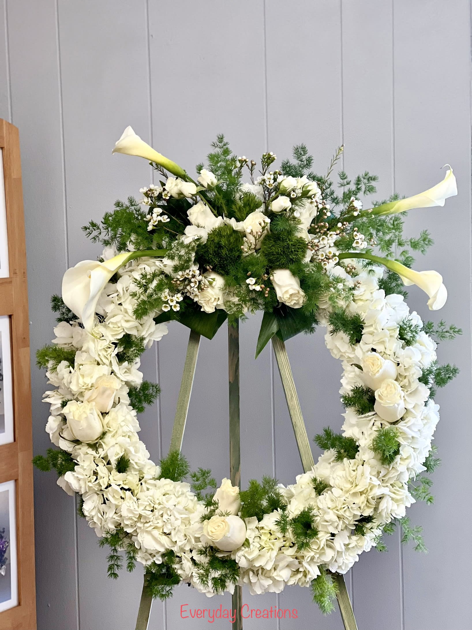 White floral wreath on an easel with calla lilies and roses