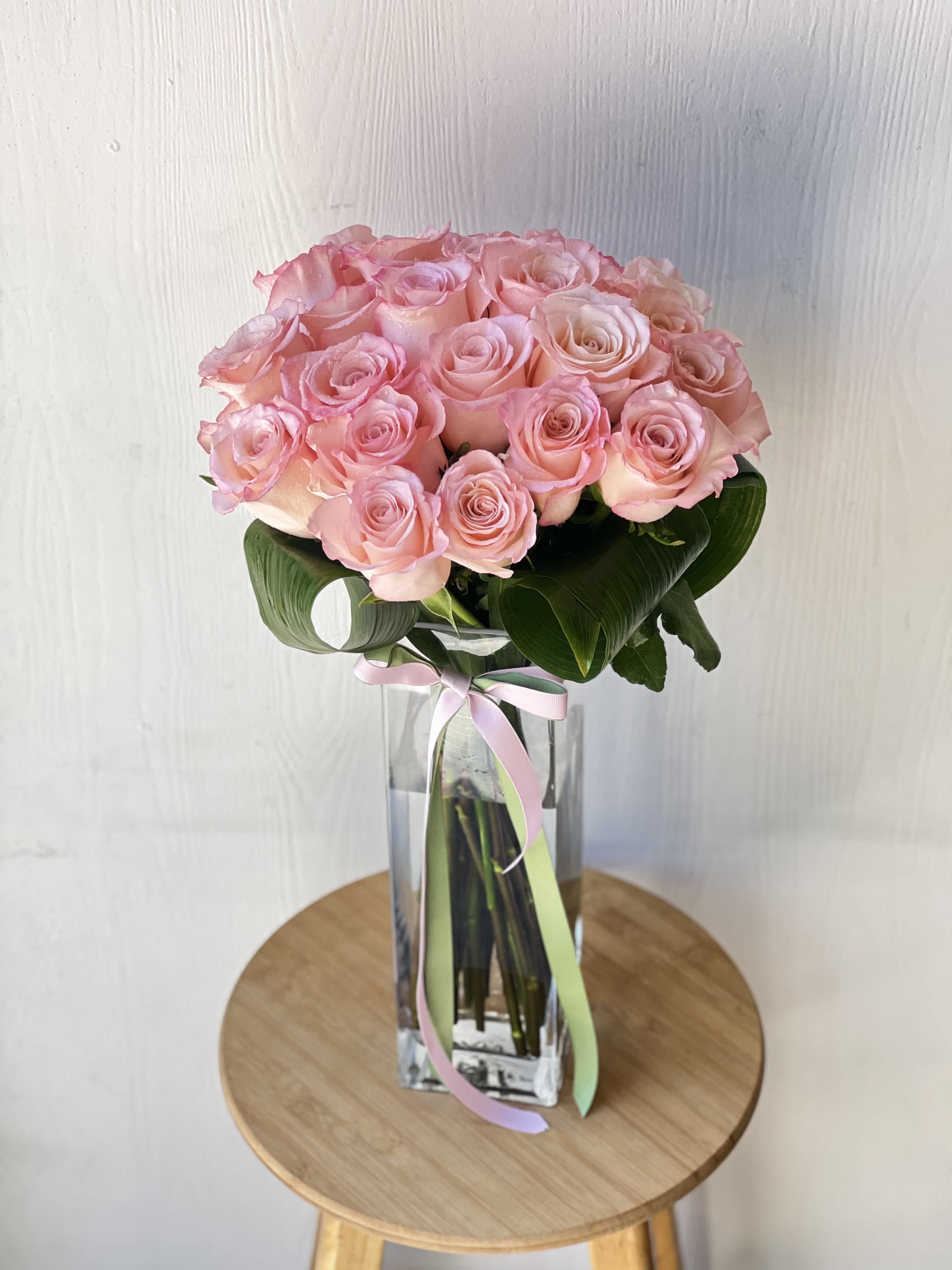 EC113 Long Stem 2 Dozen Roses - Introducing our exquisite creation that includes two dozen(strandard) pink long stem roses, elegantly bundled and adorned with a luxurious satin ribbon. Indulge in the timeless allure of these blooms, meticulously hand-selected for their delicate beauty and enchanting fragrance. Each rose, a testament to nature's artistry, exudes grace and sophistication, making it the perfect expression of admiration, affection, or celebration. Designed in a 13 inch long glass cylinder and tied with a satin ribbon, this stunning arrangement is a masterpiece of floral design, destined to captivate hearts and evoke joy. Whether it's a gesture of love, gratitude, or celebration, these roses convey sentiments that words alone cannot express.