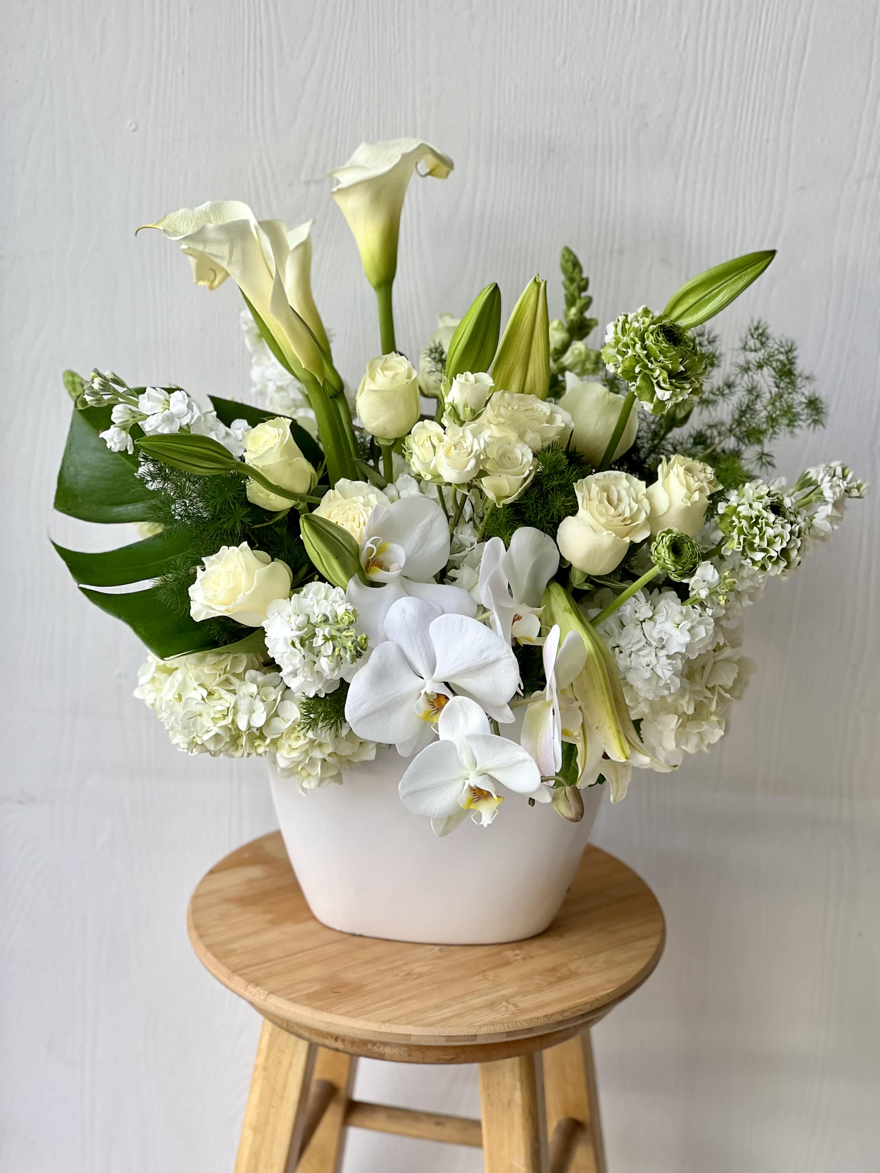 White floral arrangement in a white vase with calla lilies, roses, and orchids