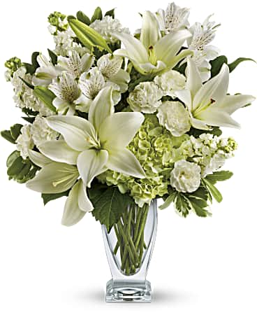 White lilies and mixed white flowers in a clear glass vase