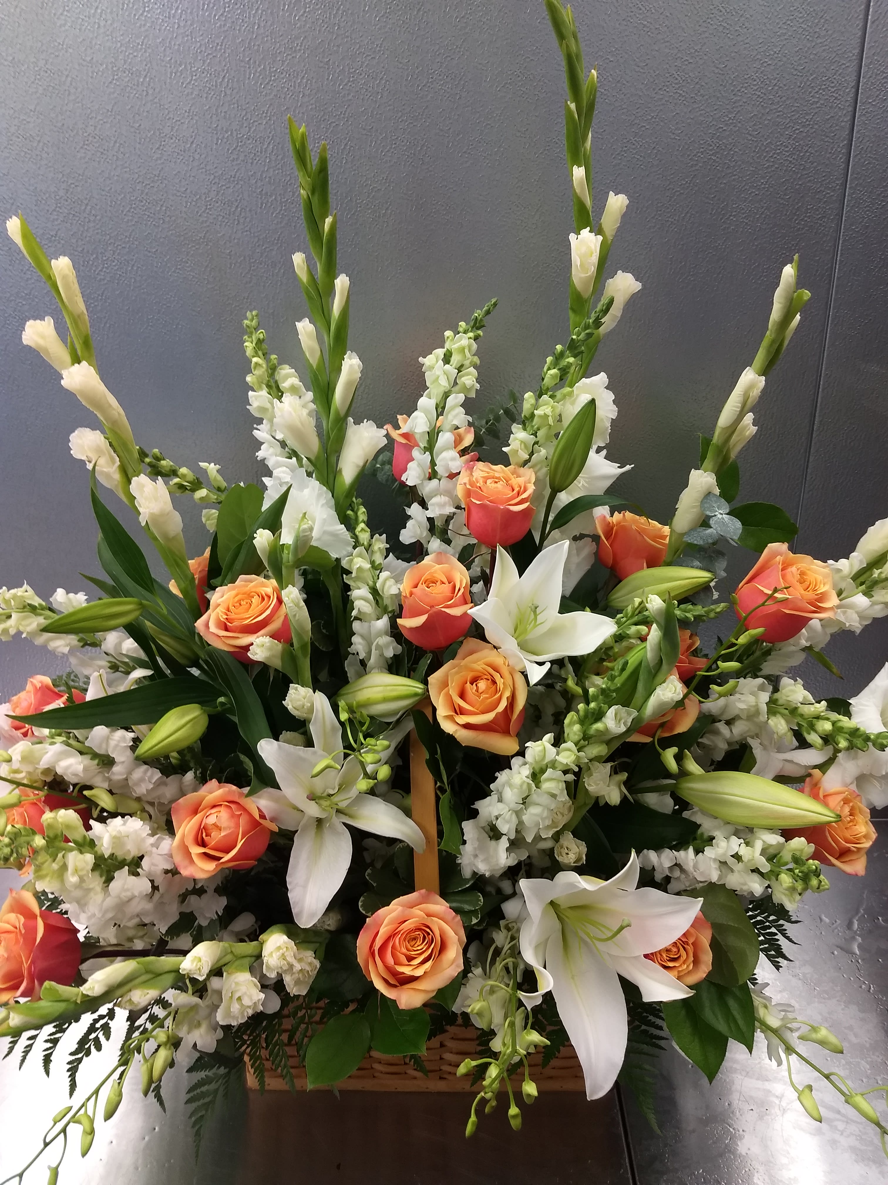 Large floral arrangement with orange roses, white lilies, and white spikes in a basket