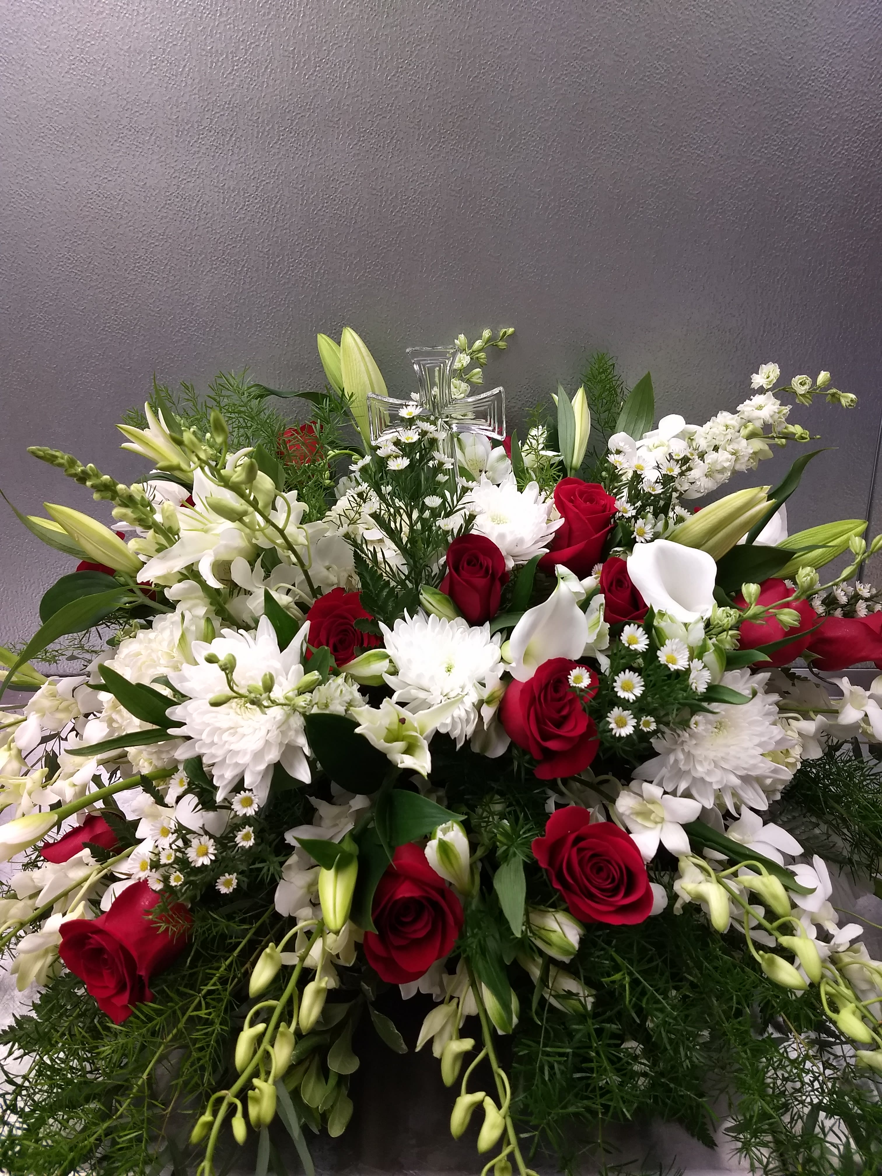 Large red and white floral spray with lilies, roses, and a clear cross topper