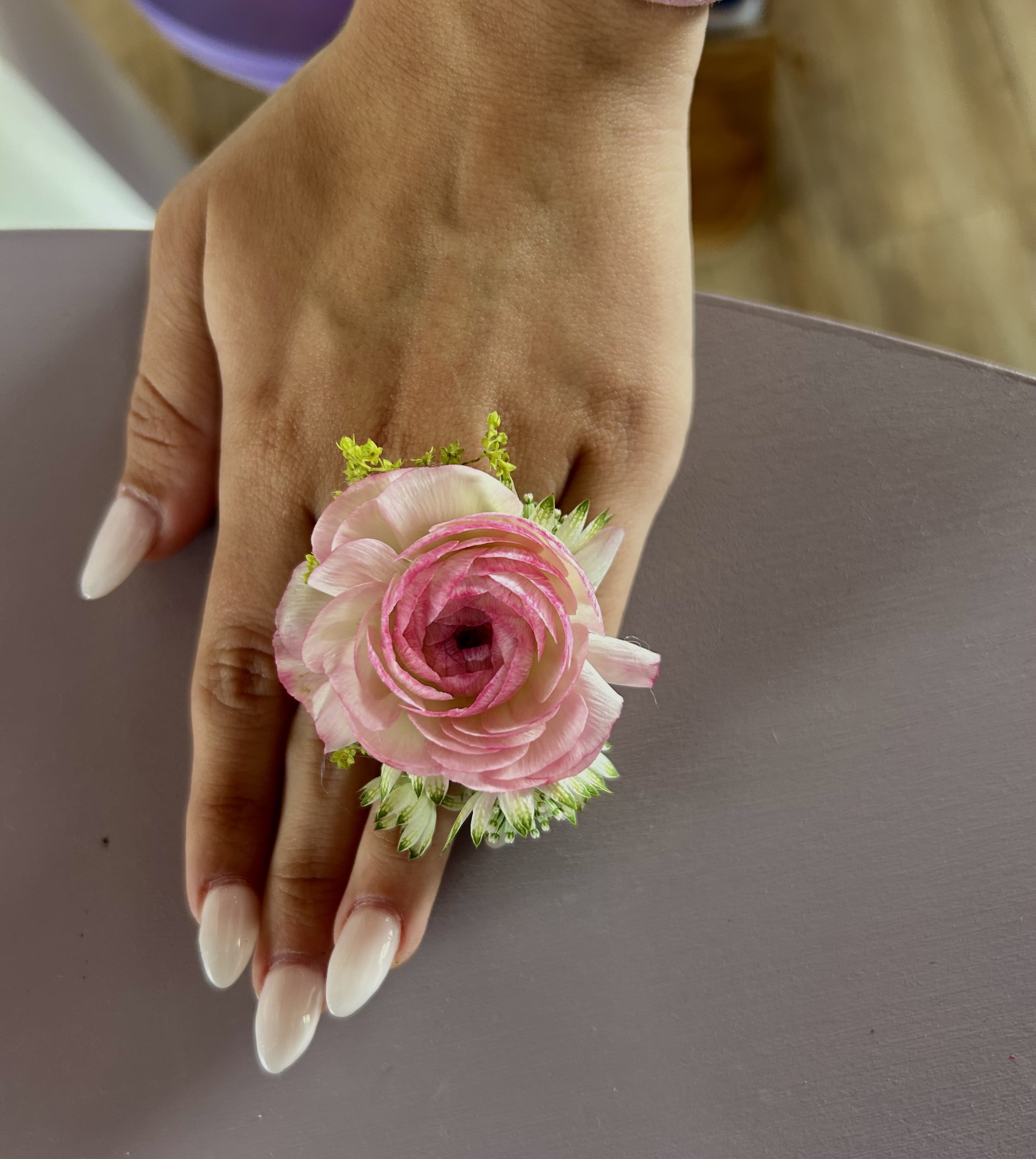 Pink ranunculus wrist corsage on a hand